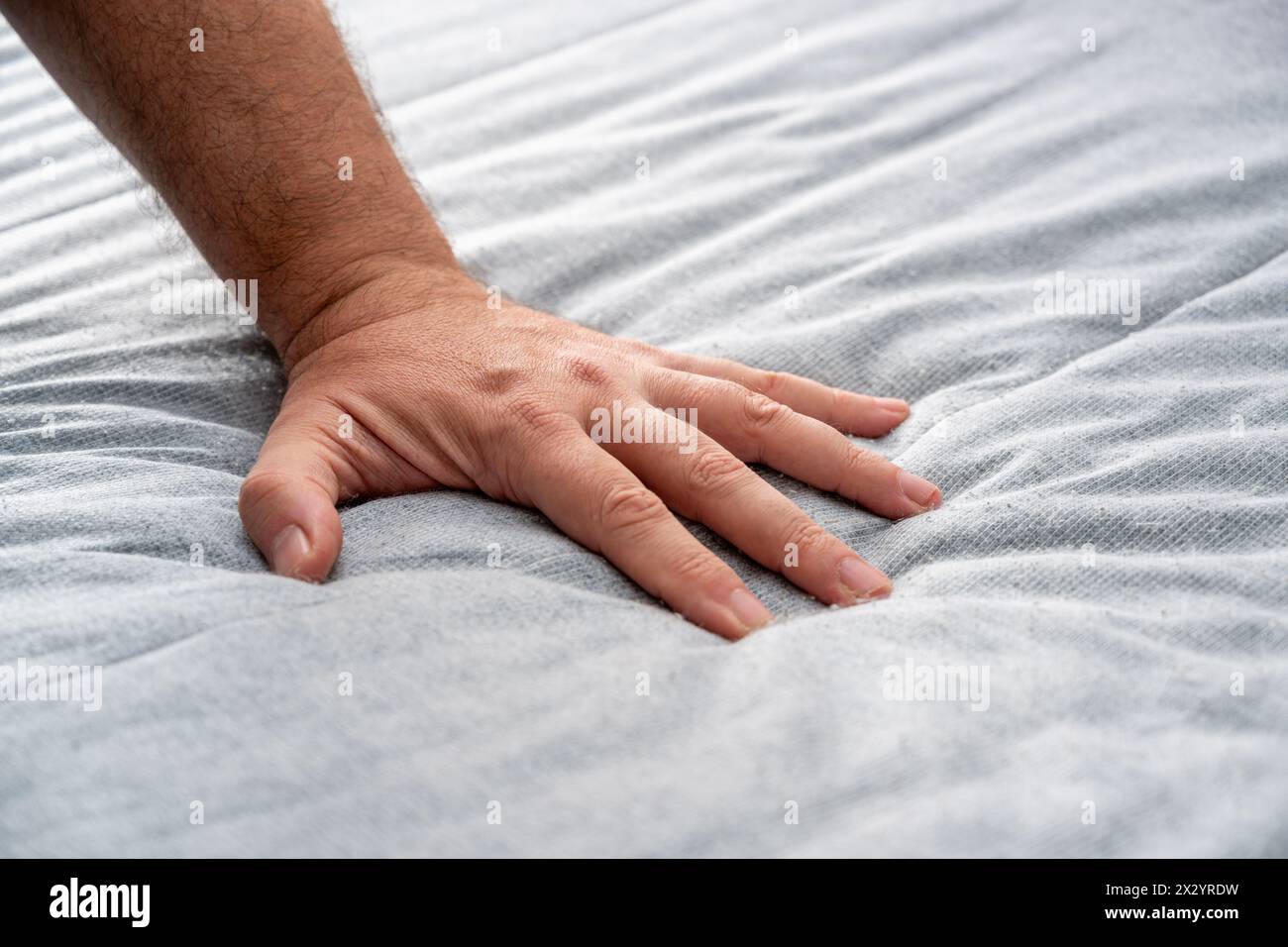 Der Mann überprüft die Qualität und Weichheit der neuen Matratze, die er kaufen wird, indem er sie mit der Hand drückt Stockfoto
