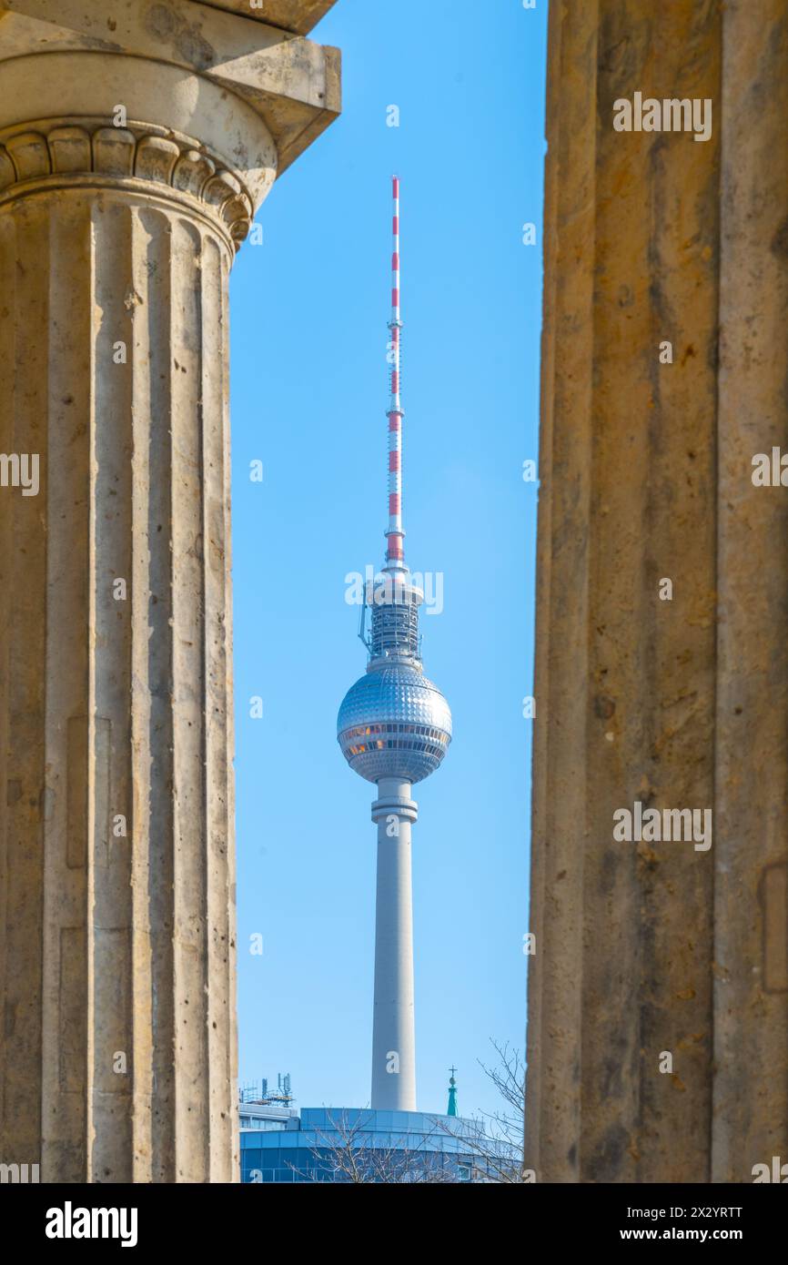 Der Berliner Fernsehturm steht hoch, eingerahmt von den klassischen Säulen eines nahe gelegenen historischen Gebäudes an klaren Tagen. Berlin, Deutschland Stockfoto