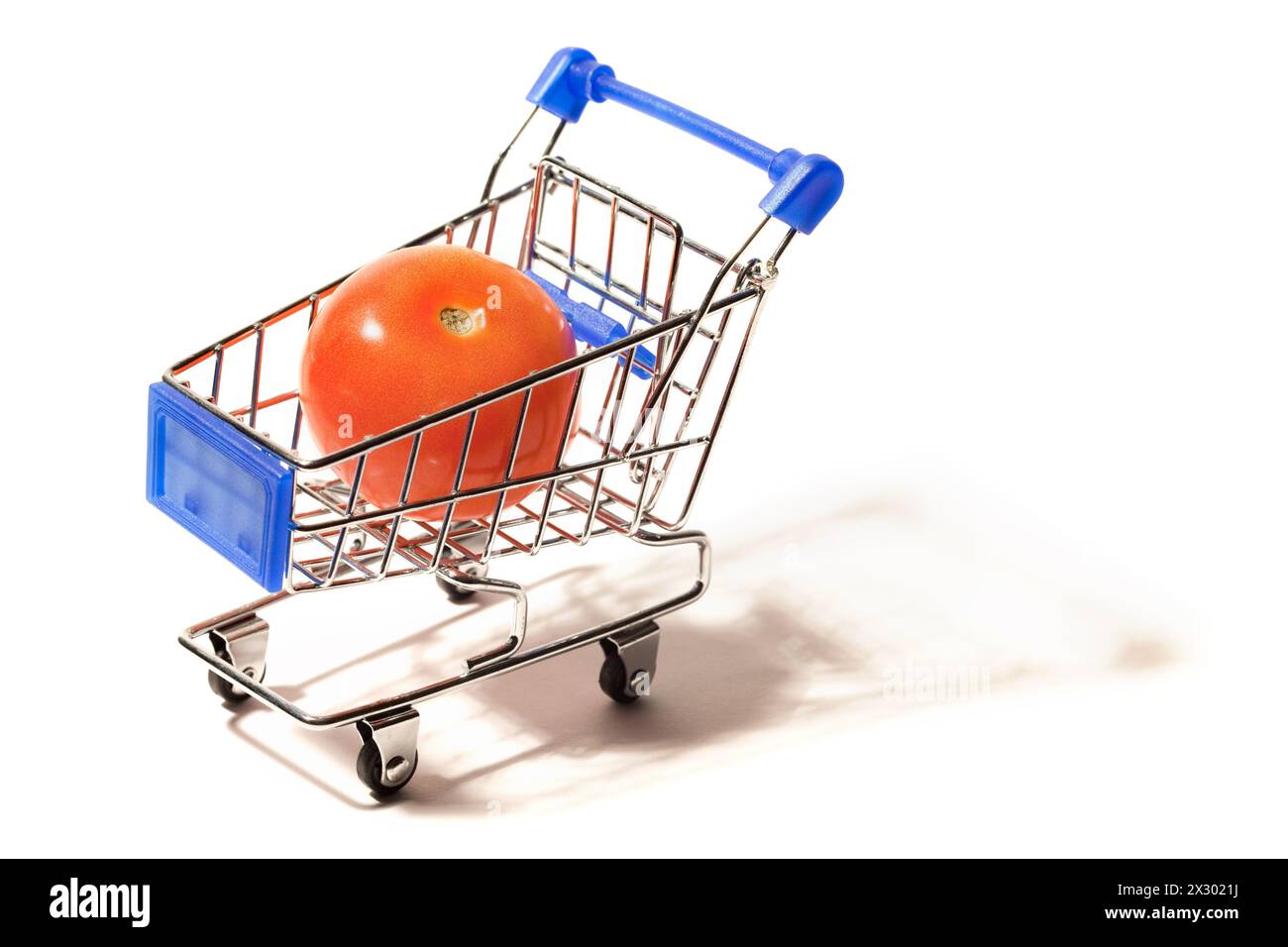 Eine große rote Tomate in einem kleinen Einkaufswagen, isoliert auf weißem Hintergrund Stockfoto