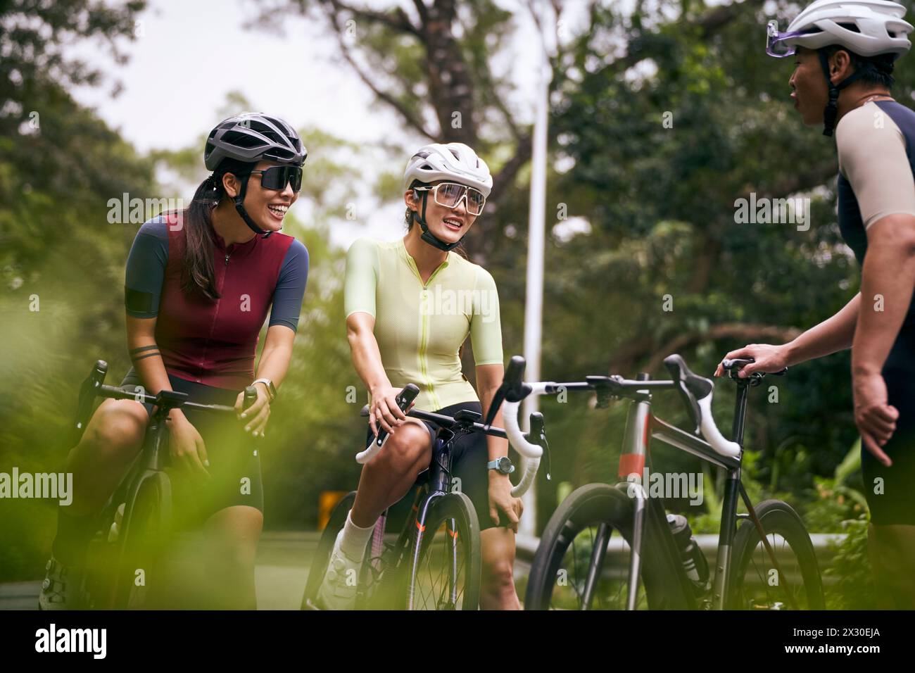 Gruppe von drei glücklichen jungen asiatischen Radfahrern, die sich unterhalten, während sie im Freien Fahrrad fahren Stockfoto