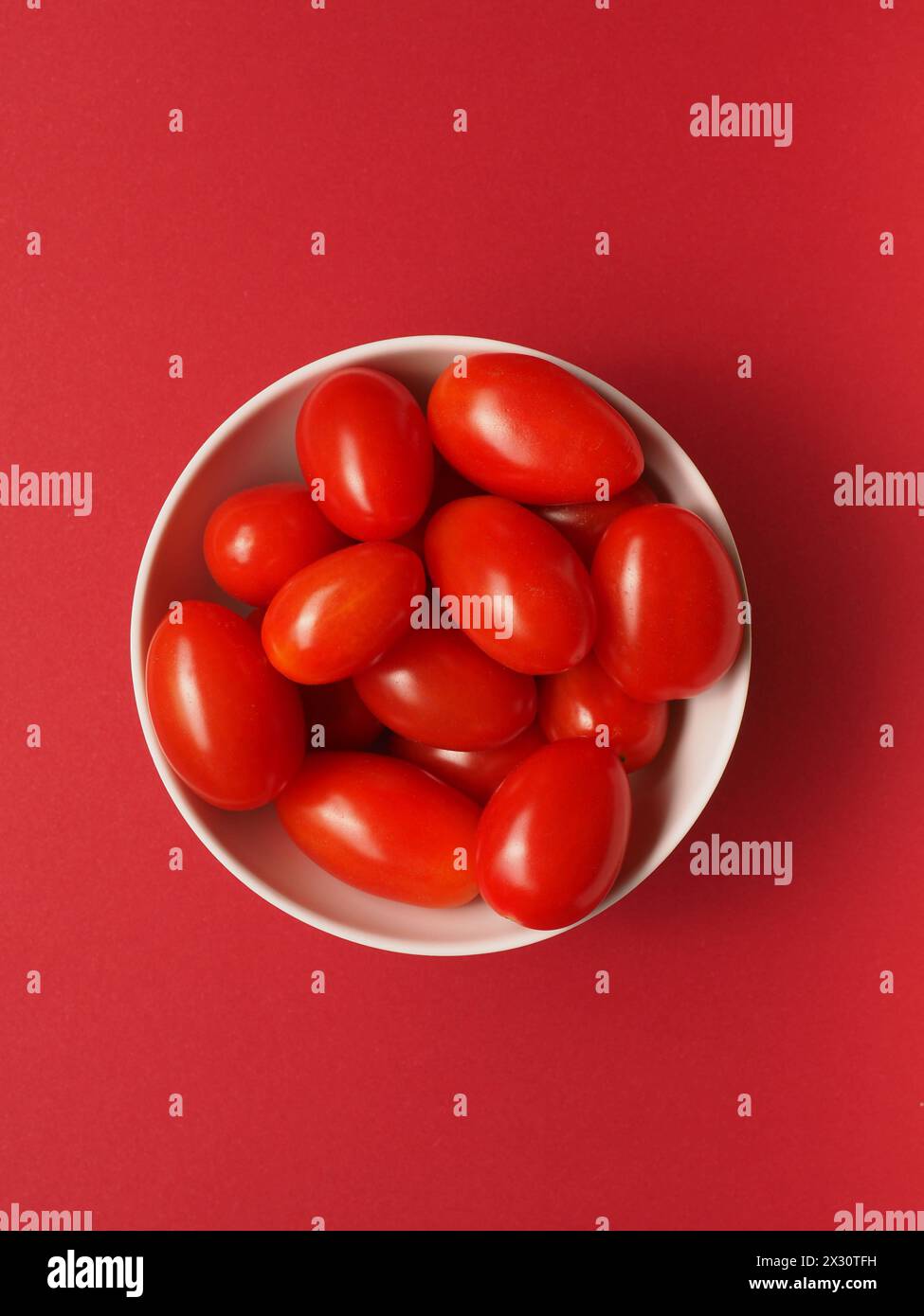 Frische Bio-Kirschtomaten in einer weißen Schüssel auf rotem Hintergrund, gesunde Lebensmittel oder Zutaten NOTIEREN DATUM NICHT ANGEGEBEN Stockfoto