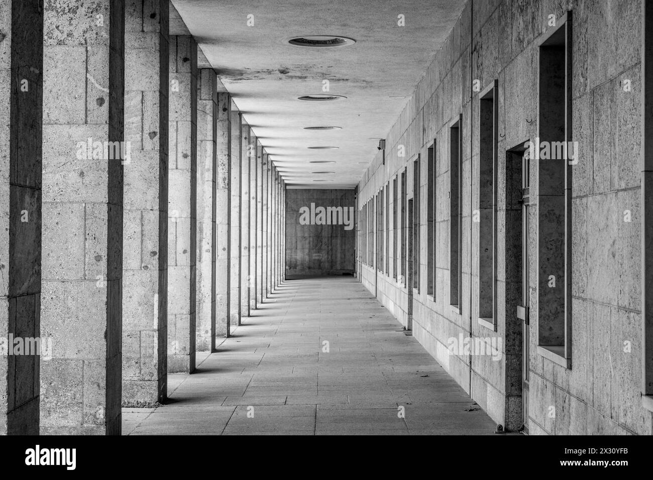 Ein verschwindender Blick auf eine moderne Arkade mit gleichmäßig verteilten Säulen und Deckenleuchten. Schwarzweißbild. Stockfoto