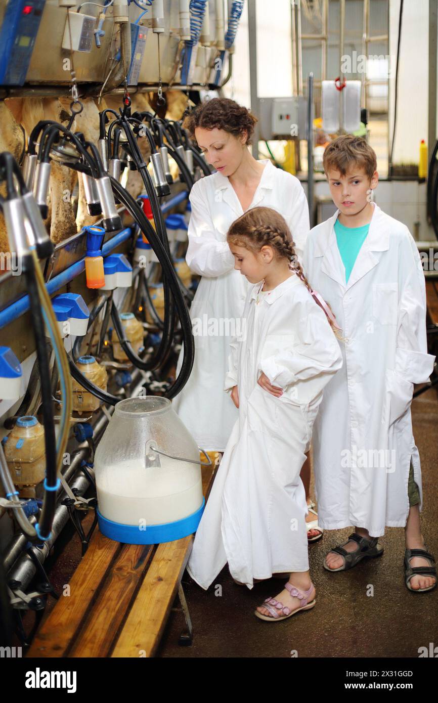 Eine dreiköpfige Familie in weißen Gewändern sieht sich neue Milch und Maschinen zum Melken von Kühen in einem großen Bauernhof an. Stockfoto