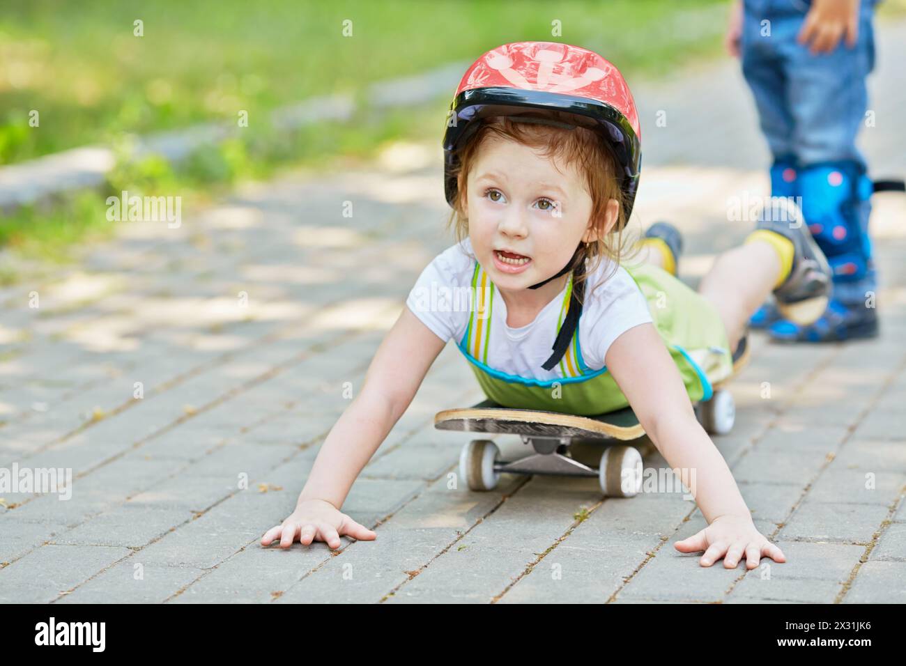 Das kleine Mädchen liegt auf dem Skateboard, Hände auf dem Boden, konzentrieren sich auf das Gesicht Stockfoto