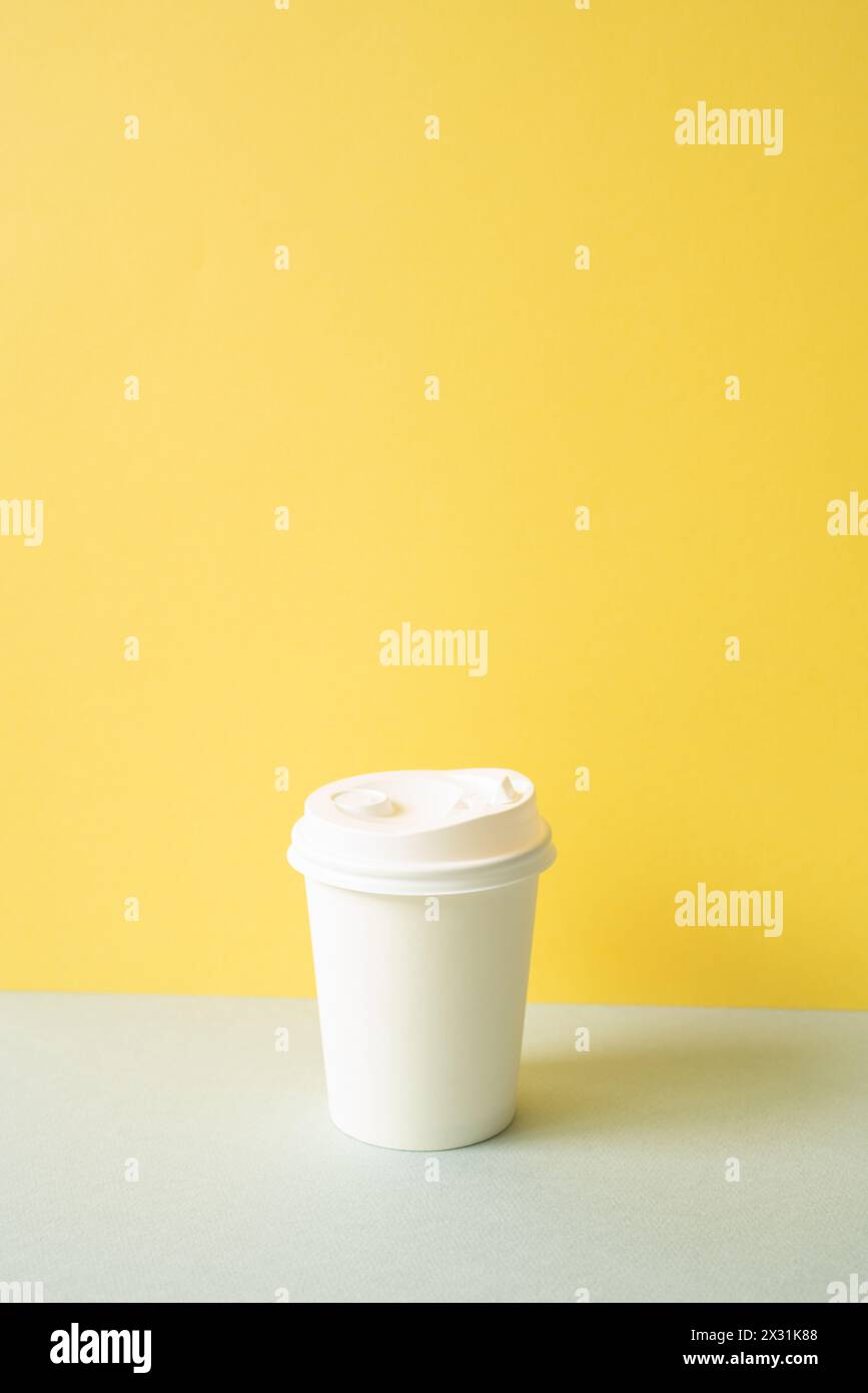Einweg-Kaffeetasse aus Papier auf grauem Tisch. Gelber Wandhintergrund Stockfoto