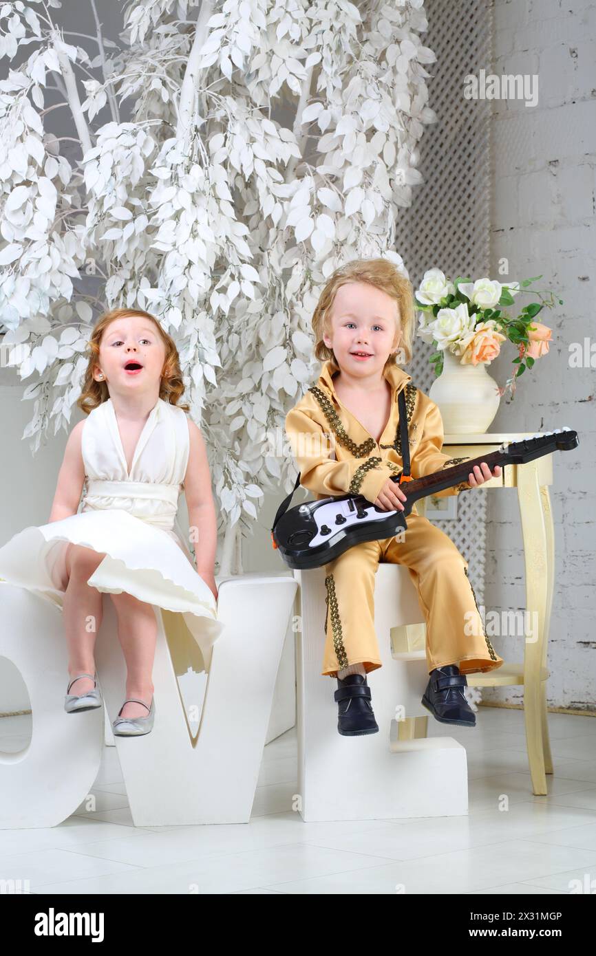 Ein kleines Mädchen in weißem Kleid und Popmusiker mit Gitarre sitzen auf Briefen und singen ein Lied Stockfoto