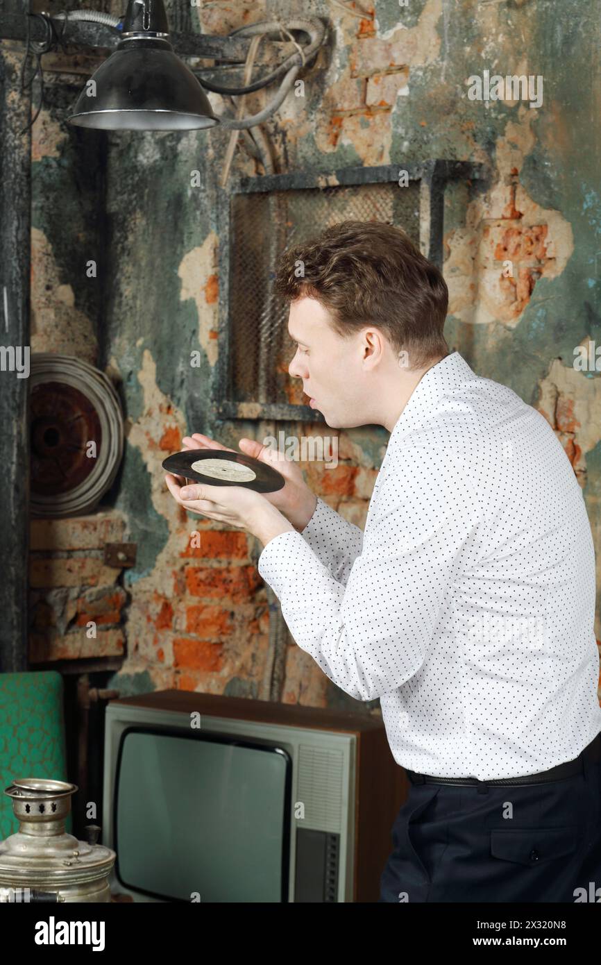 Ein Mann in weißem Hemd bläst Staub von der alten Platte in einem sehr alten Haus. Stockfoto