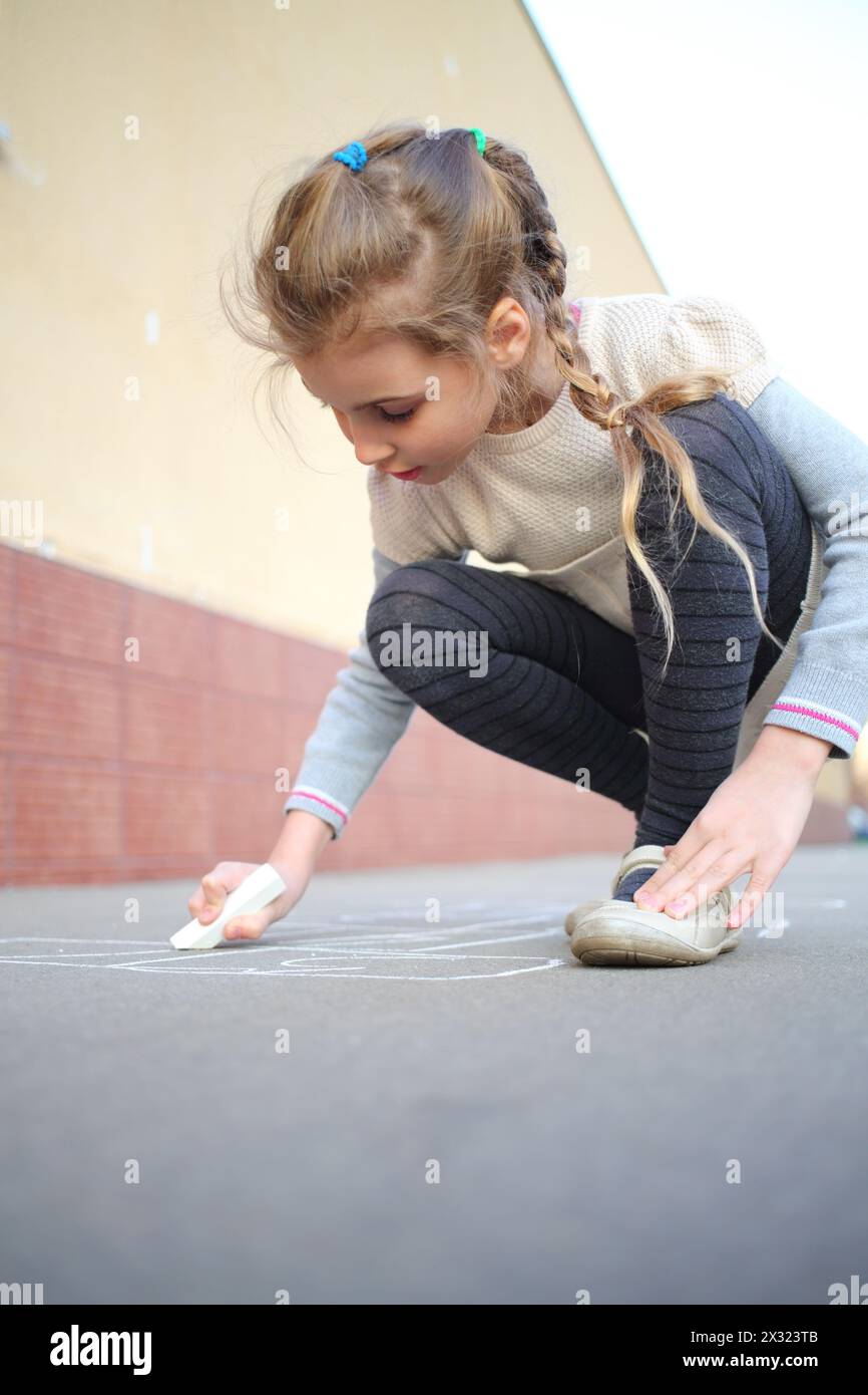 Ein lächelndes Mädchen mit Zöpfen zeichnet Hopscotch auf dem Bürgersteig Stockfoto