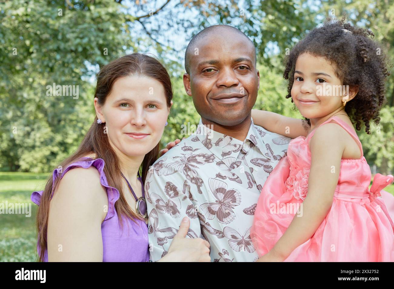 Porträt von weißer Mutter und schwarzem Vater, der kleine Tochter an den Händen hält, stehend im Sommerpark Stockfoto