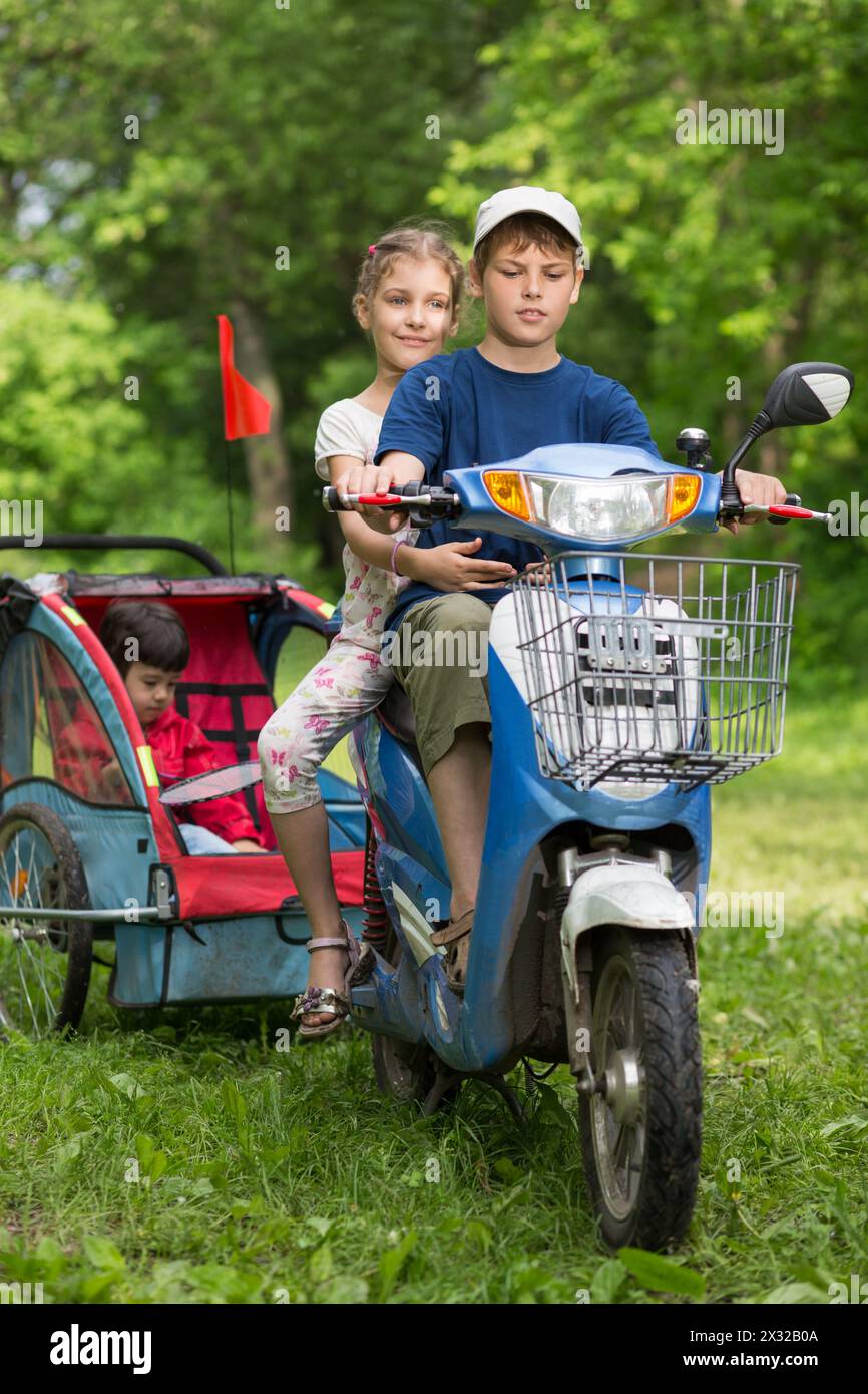 Drei Kinder auf einem Motorroller fahren in der Natur Stockfoto