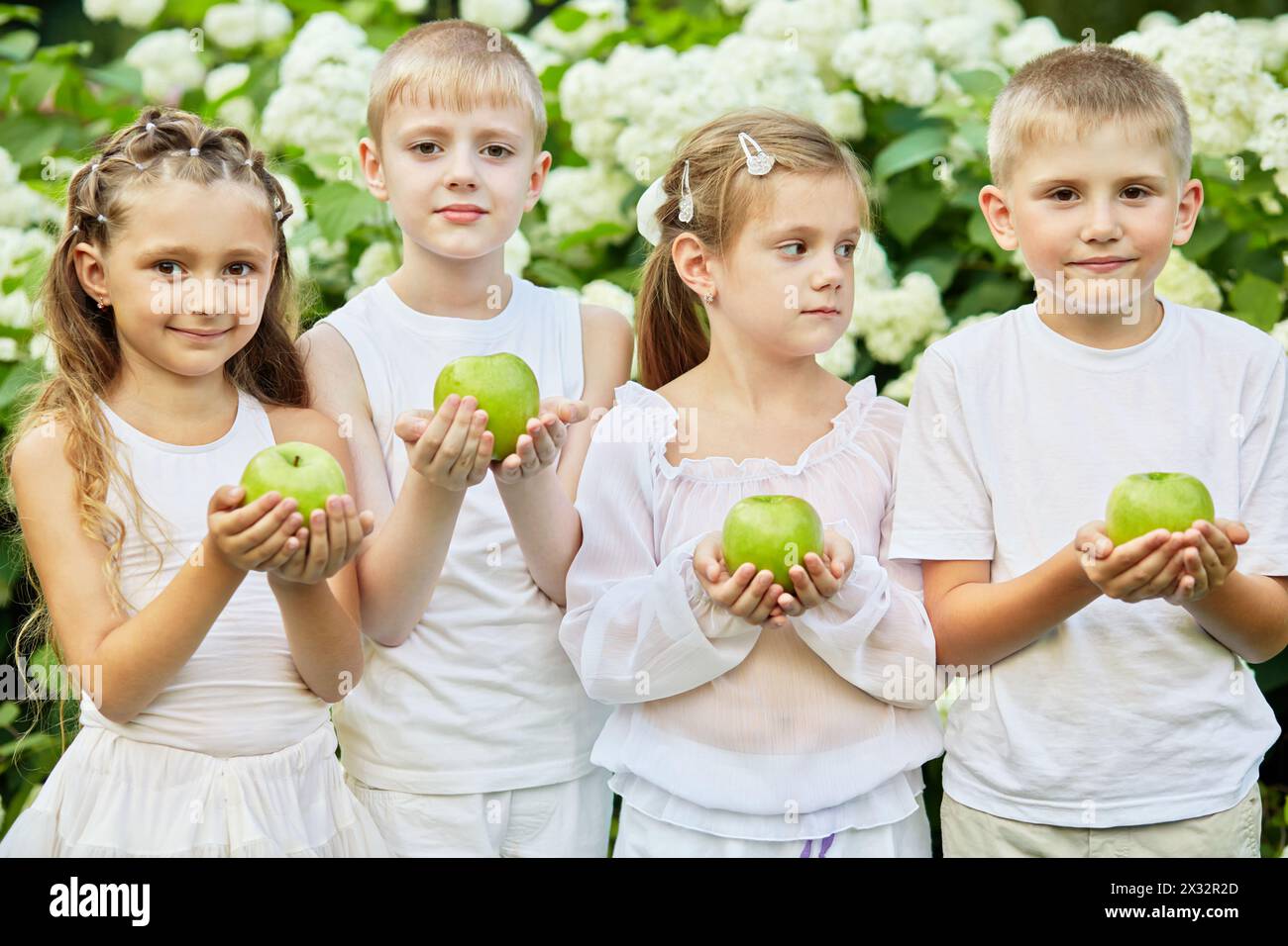 Kinder stehen vor blühenden Büschen, die grüne Äpfel in gefalteten Palmen halten Stockfoto