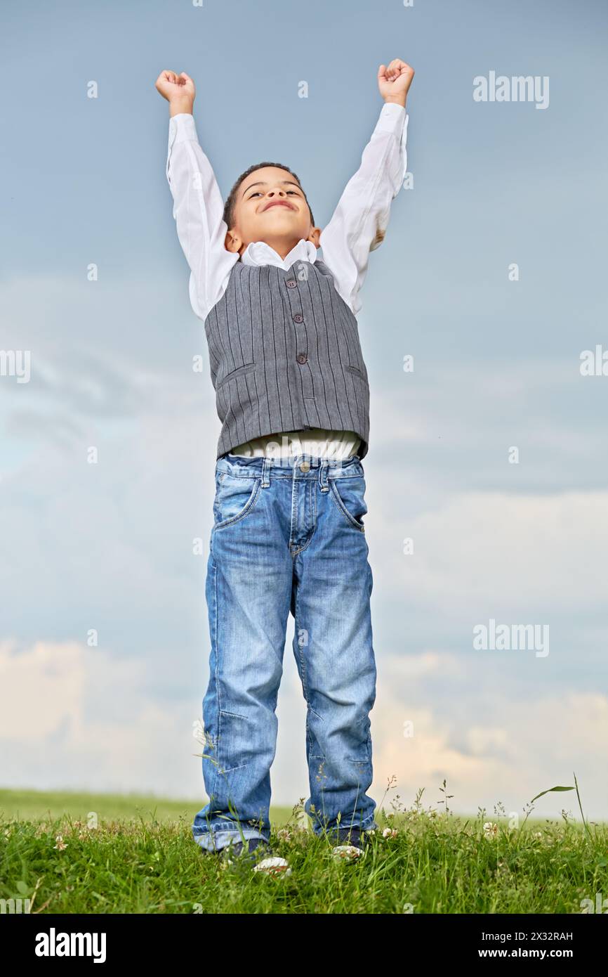 Porträt eines Mulatten-Jungen, der mit erhobenen Händen gegen bewölkten Himmel steht Stockfoto