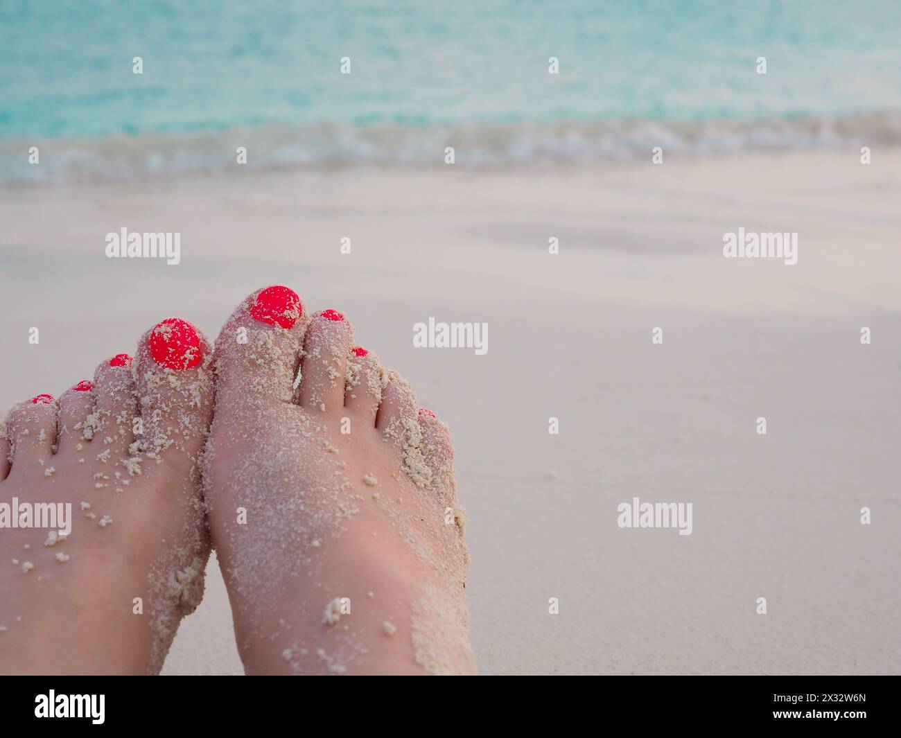Damenfüße mit bemalten Zehennägeln an einem verlassenen weißen Sandstrand auf den Malediven mit türkisfarbenem Meer dahinter. Entspannter Urlaub. Platz zum Kopieren Stockfoto