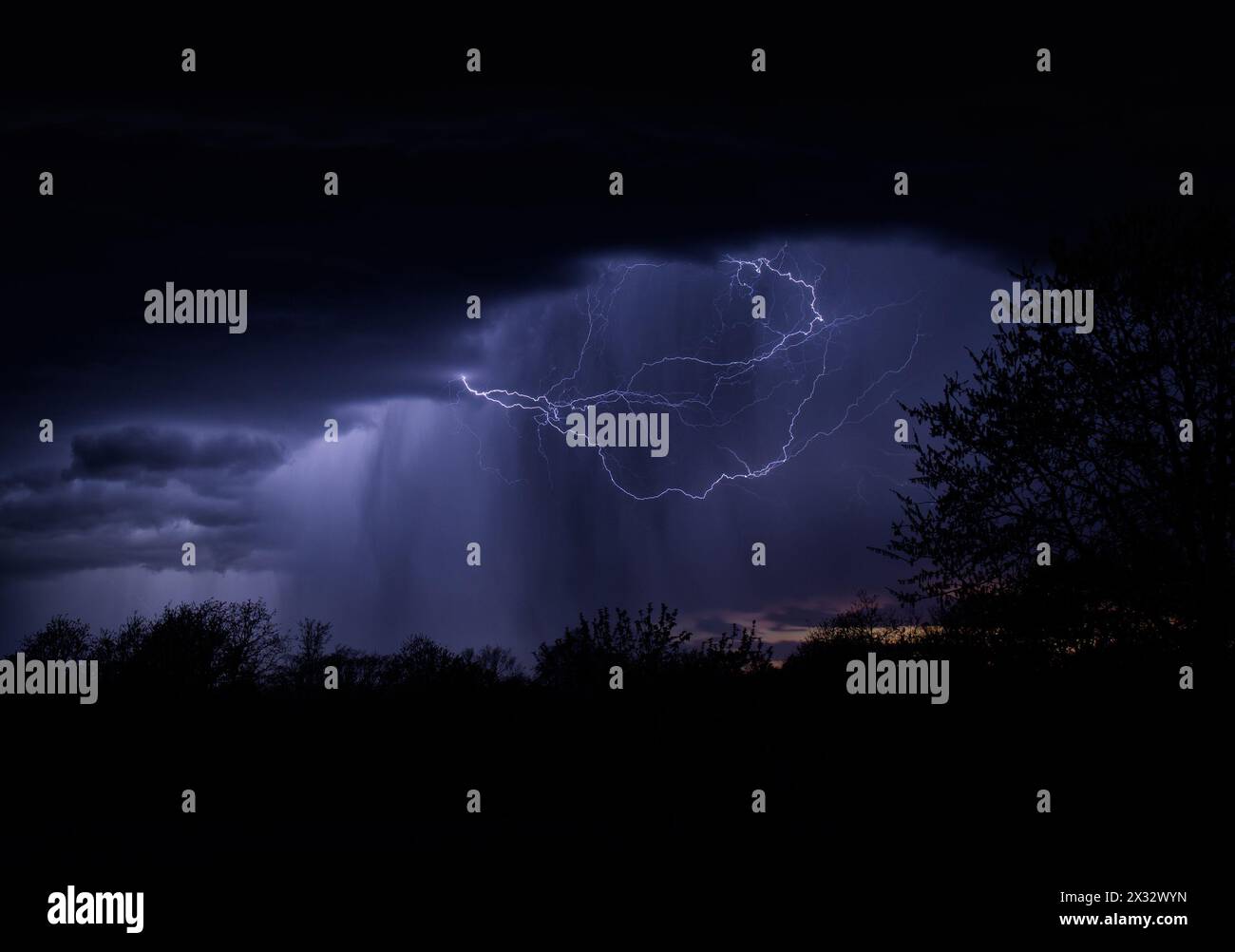 Wolken-Luft-Blitze beleuchten einen Regenschacht, der nachts aus der Sturmwolke strömt Stockfoto