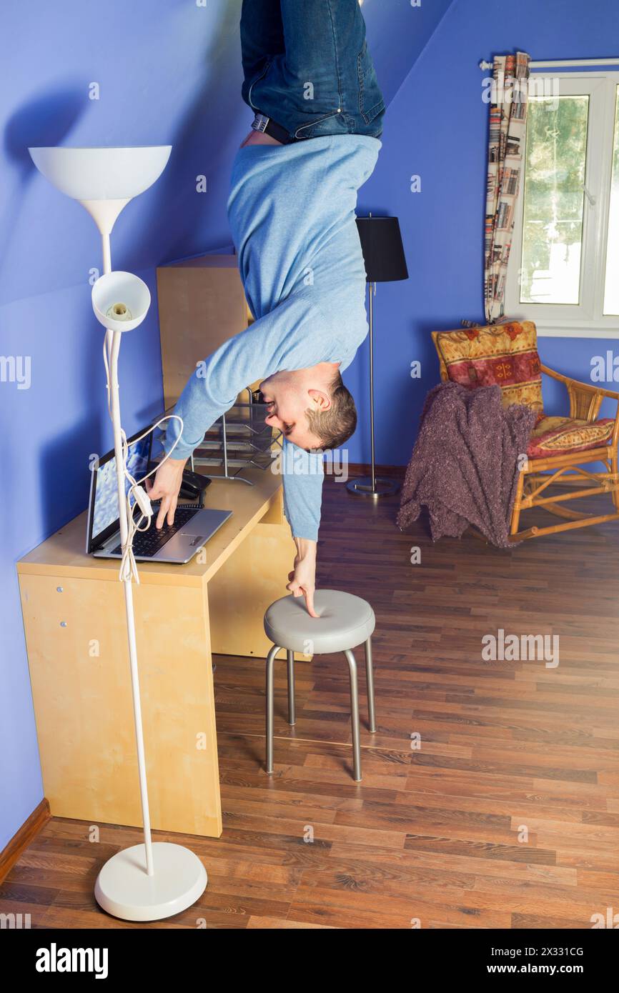 Mann in Jeans, der kopfüber unter dem Tisch steht, mit Computer Stockfoto