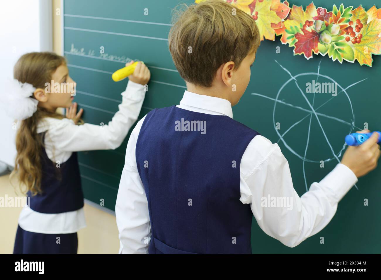 Der Junge zeichnet und das Mädchen schreibt auf die Tafel in der Schule. Stockfoto