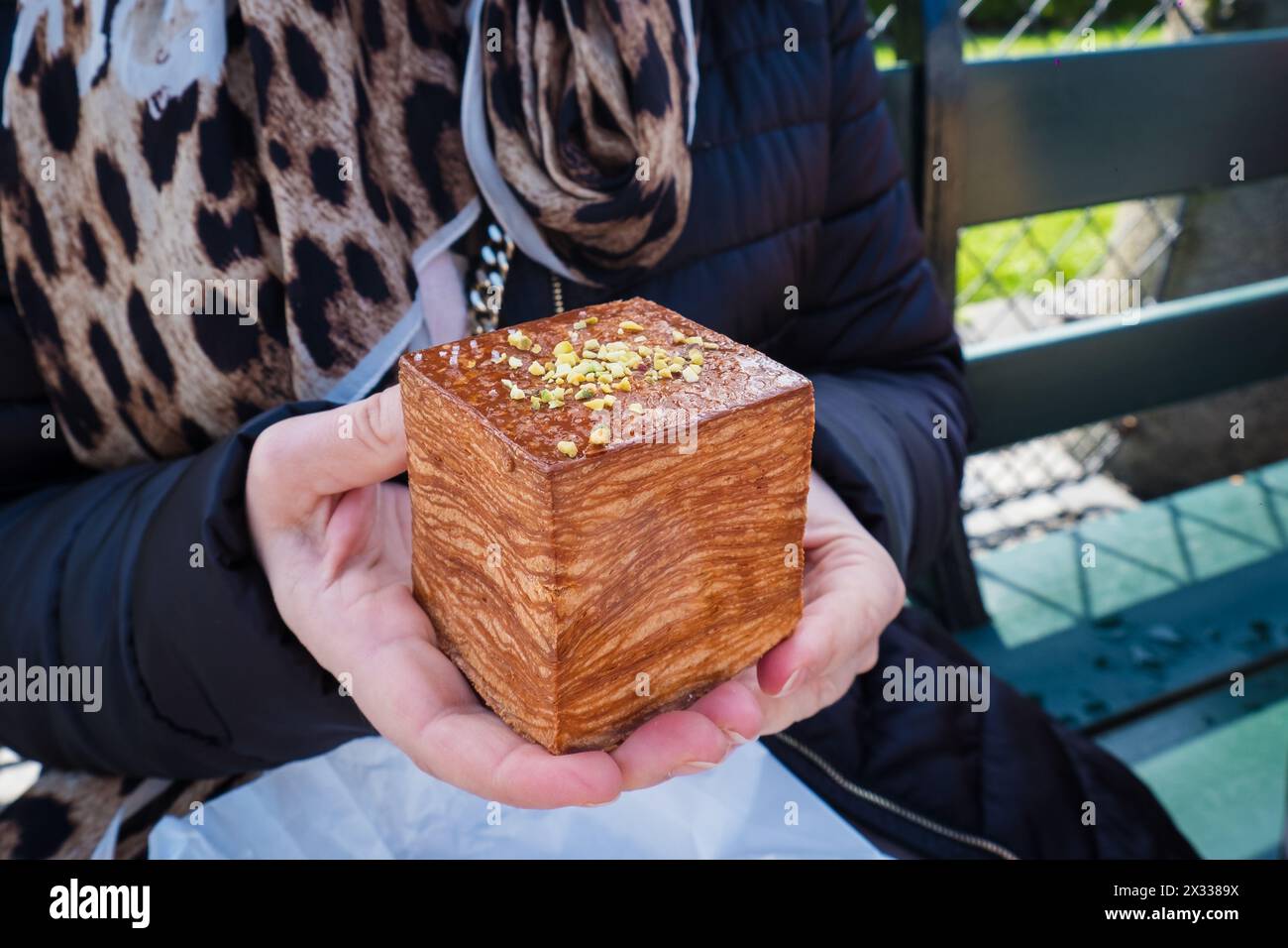 Eine Frau, die ein frisches würfelförmiges Croissant mit Pistazien-Ganache-Füllung hält. Stockfoto