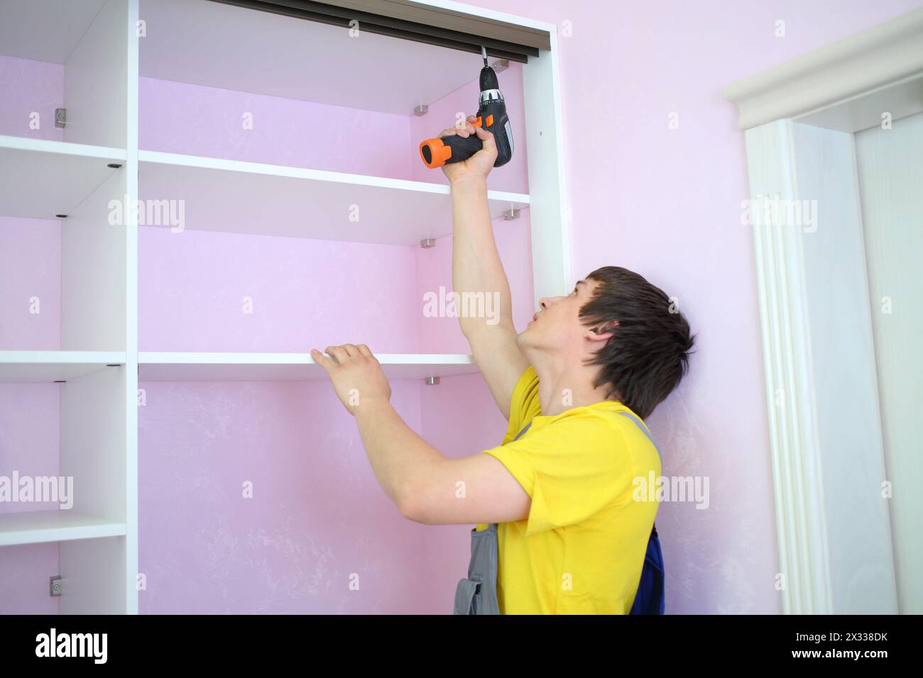 Mann, der Führungsschienen für den Schiebeschrank in einem Raum mit rosafarbenen Wänden installiert Stockfoto