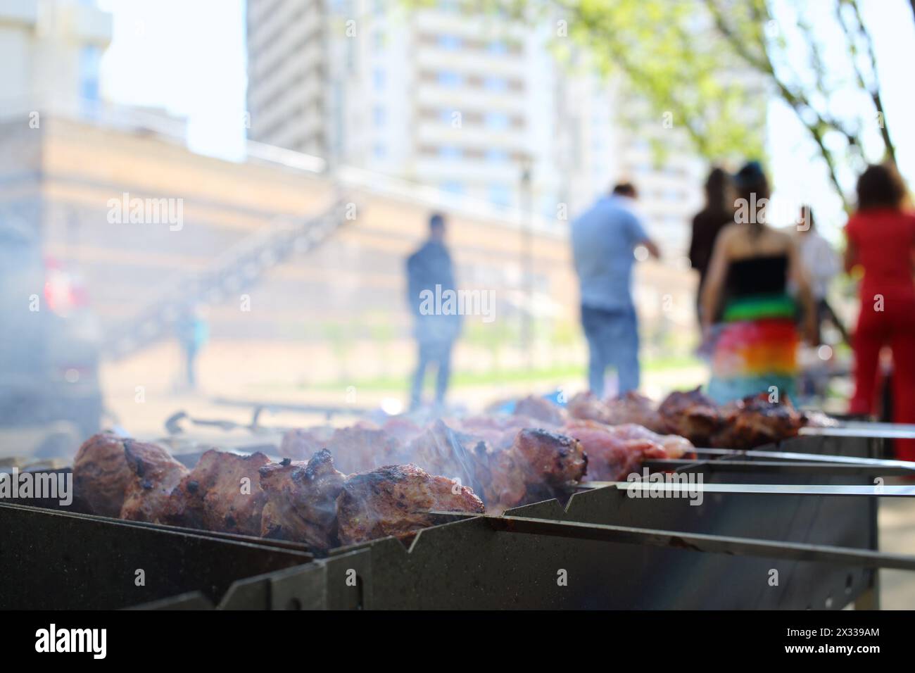 Nahaufnahme des Barbecue mit Fleischscheiben auf Spießen vor den Leuten Stockfoto