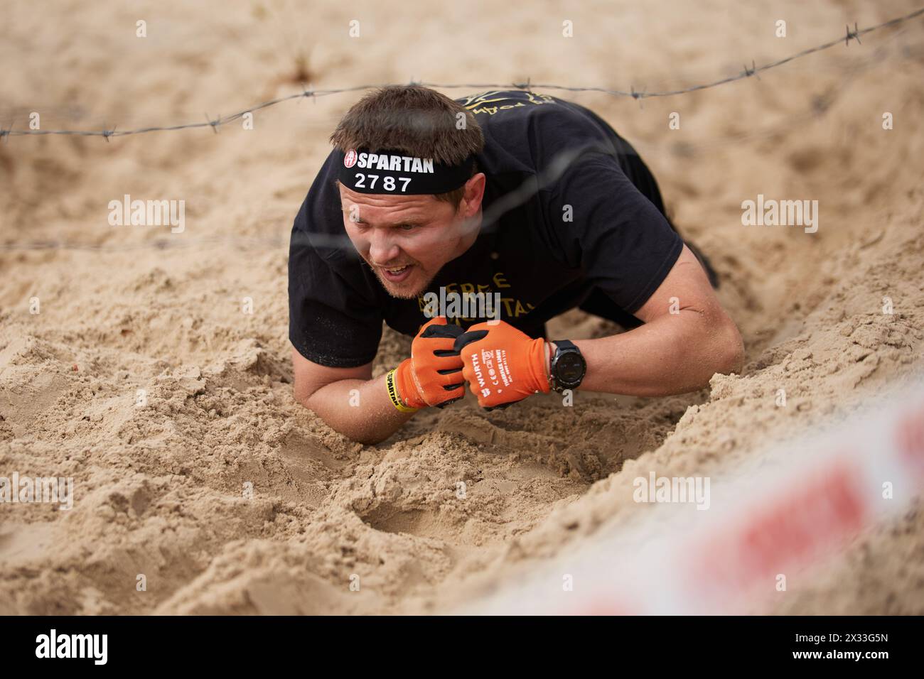 Ukrainischer Mann krabbelte auf Sand unter dem Stacheldraht während des Spartan Race Wettbewerbs in Kiew am 20. April 2024 Stockfoto