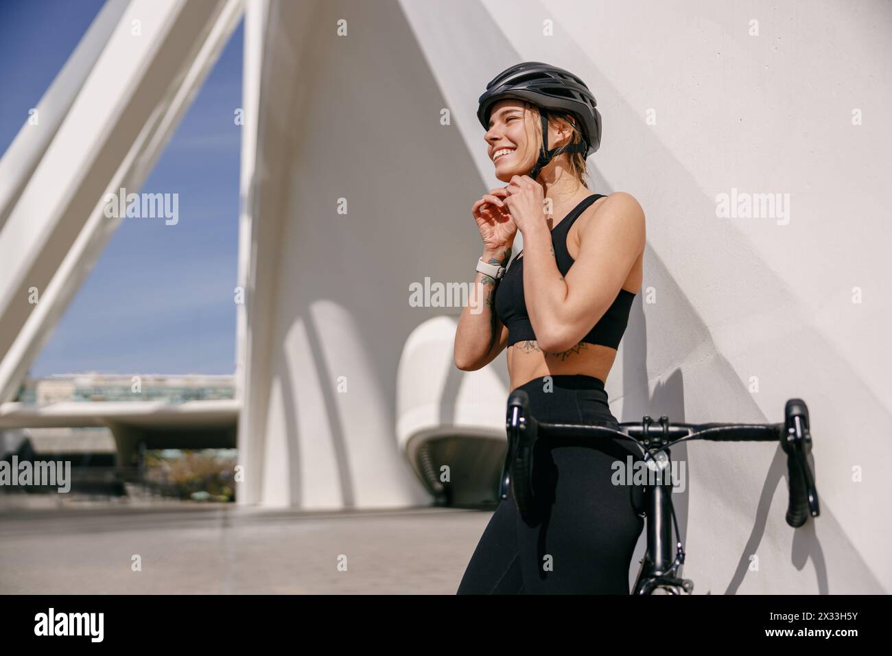 Lächelnde Radfahrerin legt Helm auf den Kopf, bevor sie in der Stadt mit dem Fahrrad fahren geht Stockfoto