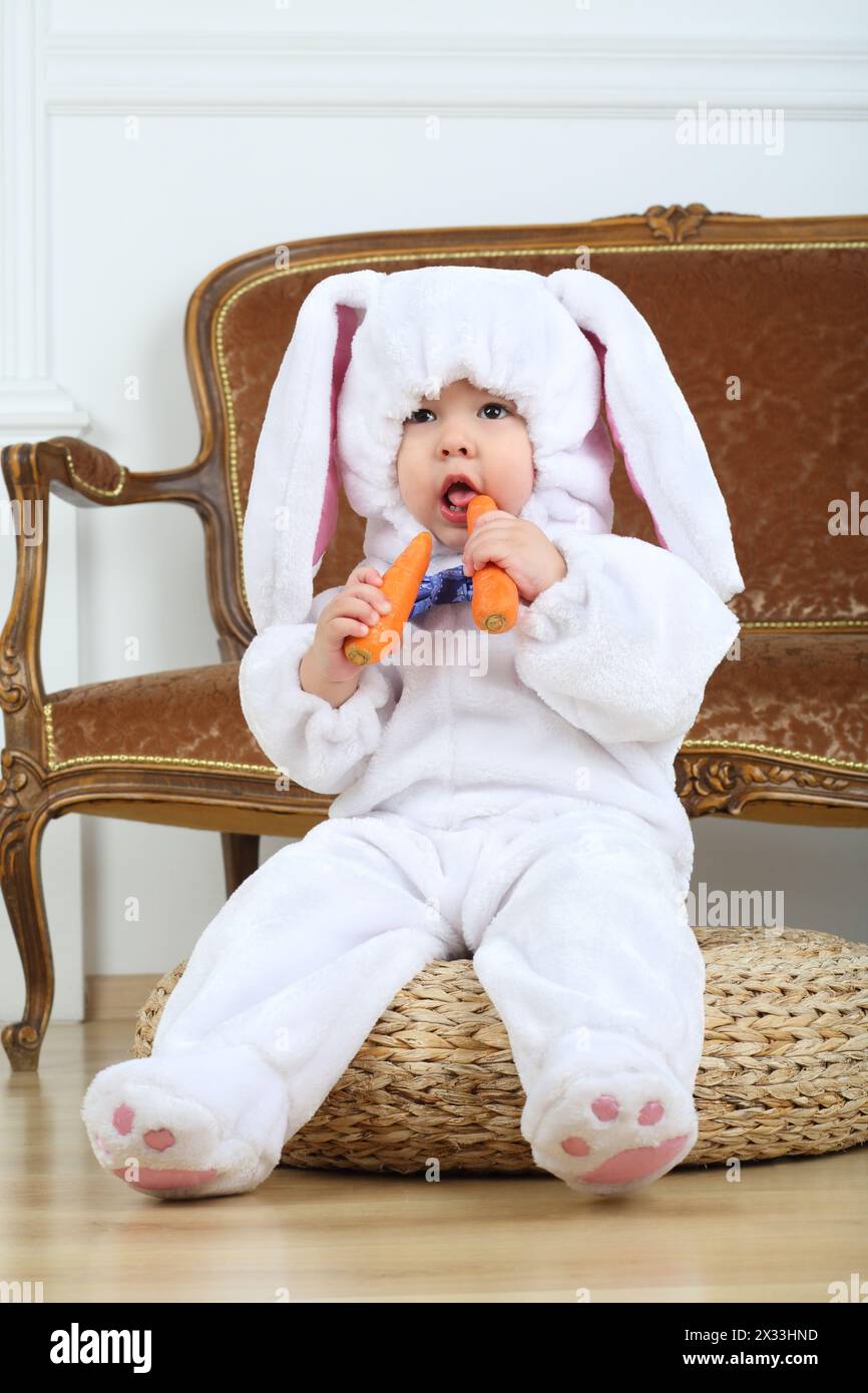 Kleiner Junge im Kostümhase, der auf dem Hocker mit Karotten sitzt Stockfoto