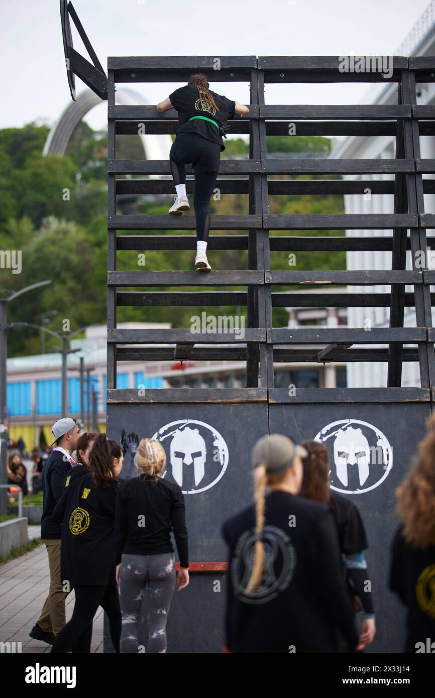 Frauen klettern auf einem hohen hölzernen A-förmigen Hindernis in einer Disziplin „Treppenweg nach sparta“ beim Spartan Race Competition in Kiew - 20. April 2024 Stockfoto