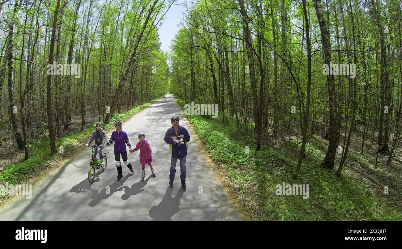 Vier Personen Eltern und Kinder fahren am sonnigen Frühlingstag auf Rollerblades und mit dem Fahrrad auf der Straße durch den Wald. Luftaufnahme Stockfoto
