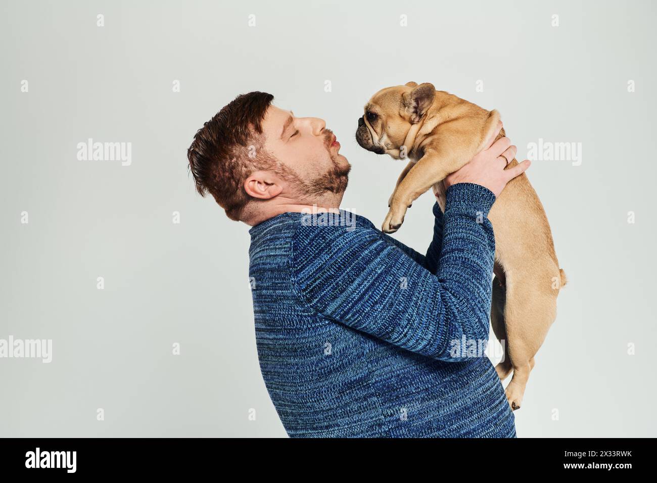 Ein Mann hält liebevoll eine französische Bulldogge ins Gesicht. Stockfoto