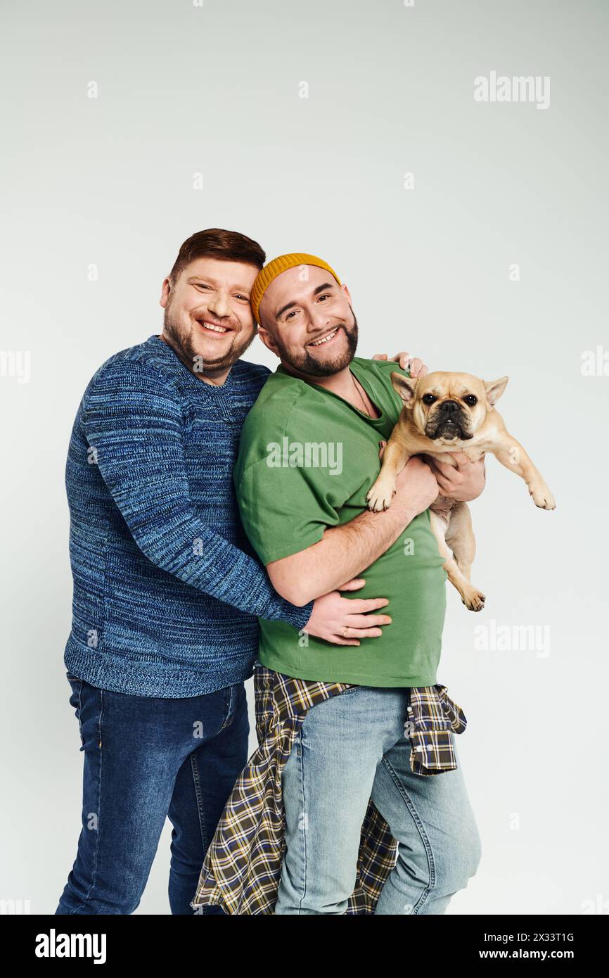 Zwei Männer umarmen sich, während sie eine süße französische Bulldogge halten. Stockfoto