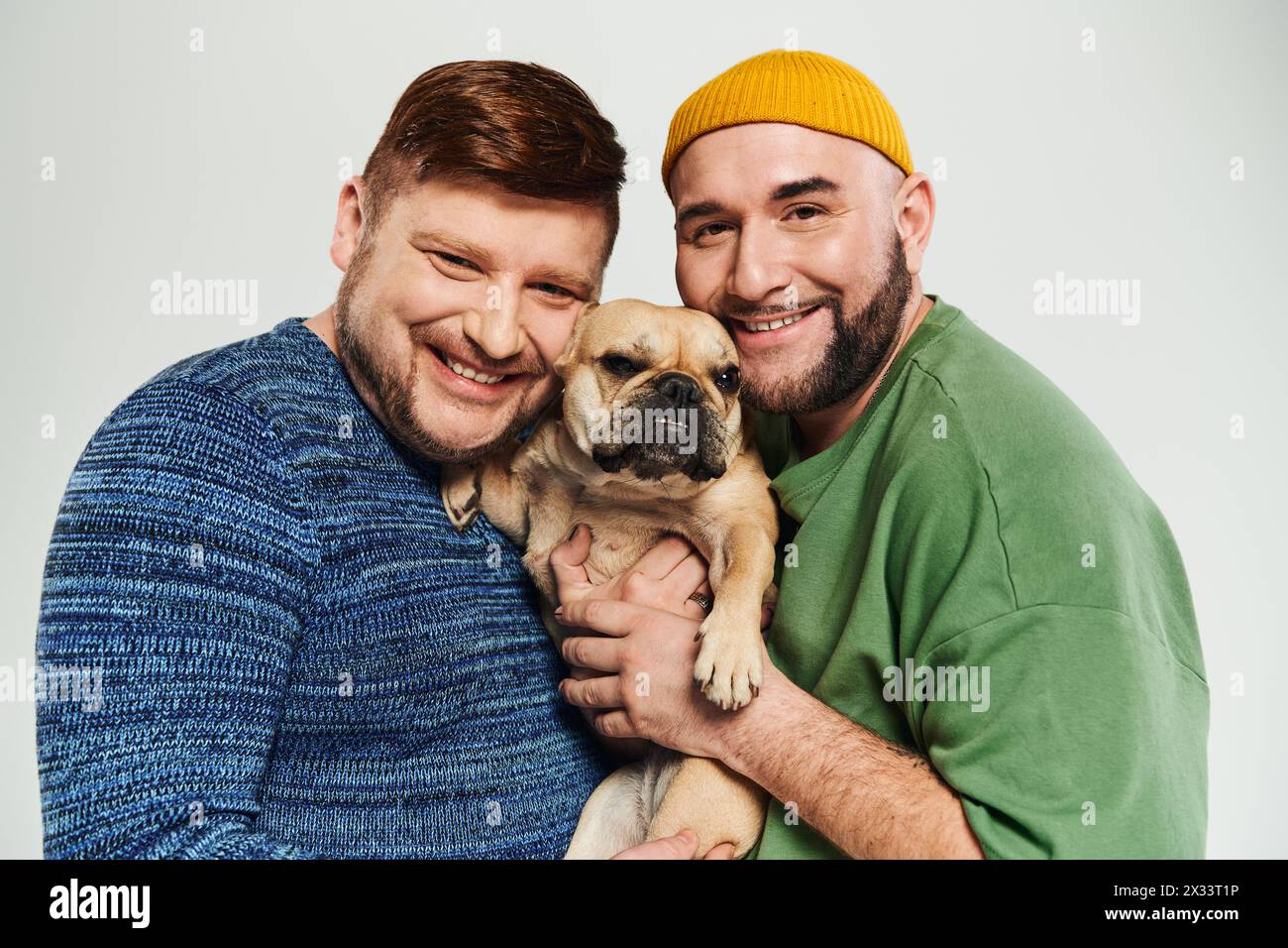 Ein liebevolles schwules Paar, das ihre kleine französische Bulldogge mit Sorgfalt und Zuneigung hält. Stockfoto