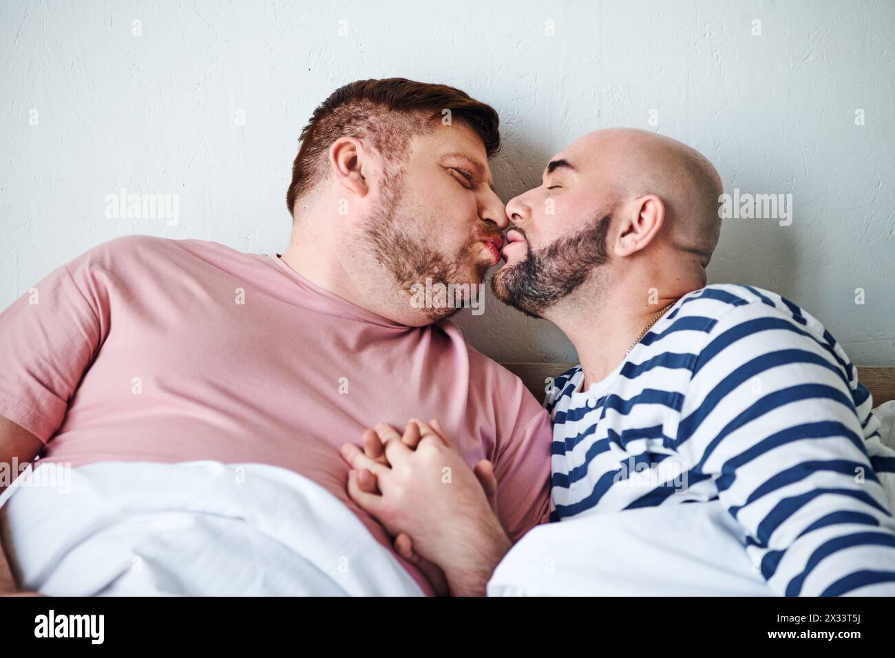 Ein paar Männer liegen im Bett und teilen sich einen zarten Kuss. Stockfoto