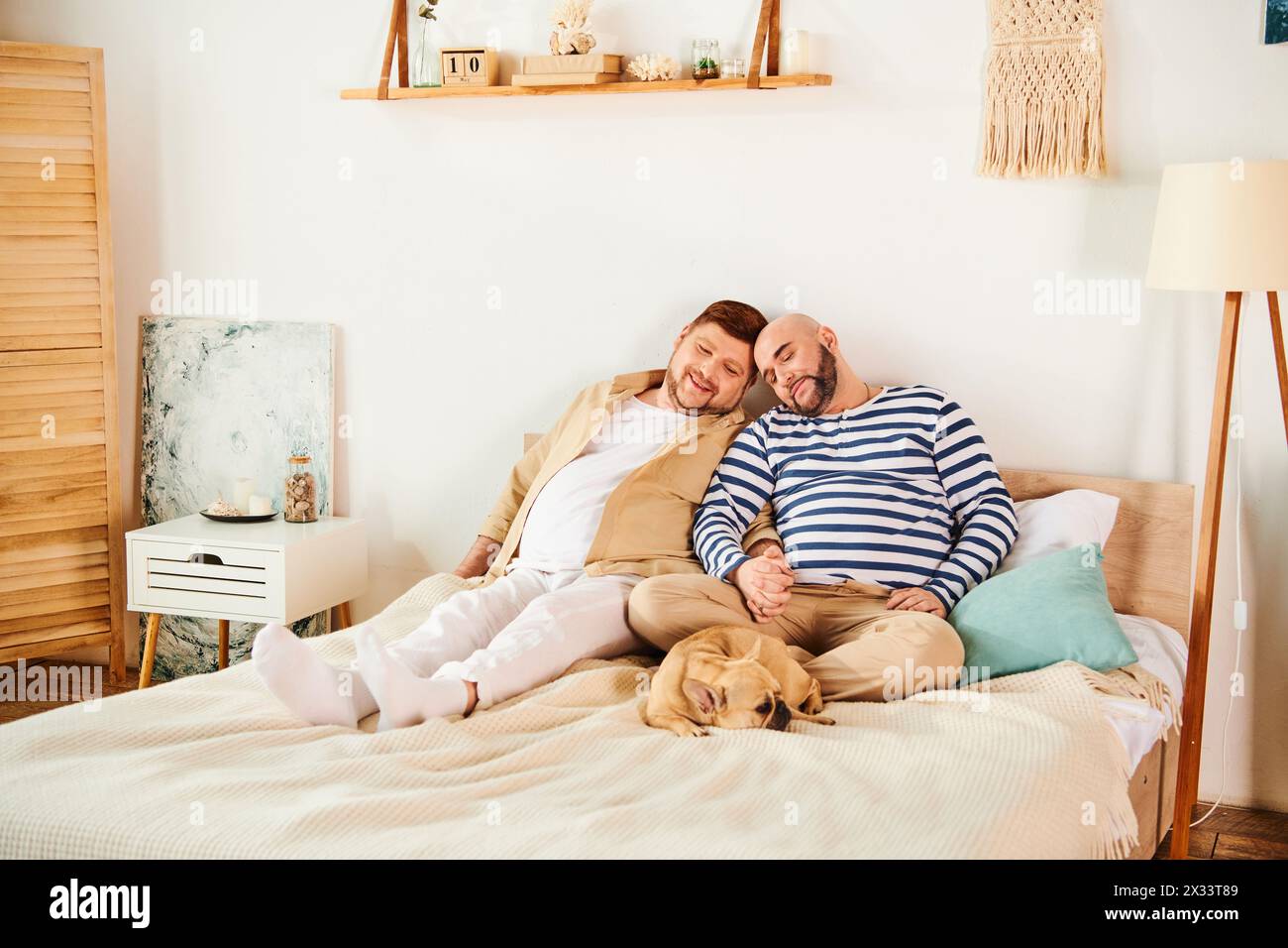 Ein schwules Paar, neben ihrer französischen Bulldogge, die auf einem Bett liegt. Stockfoto