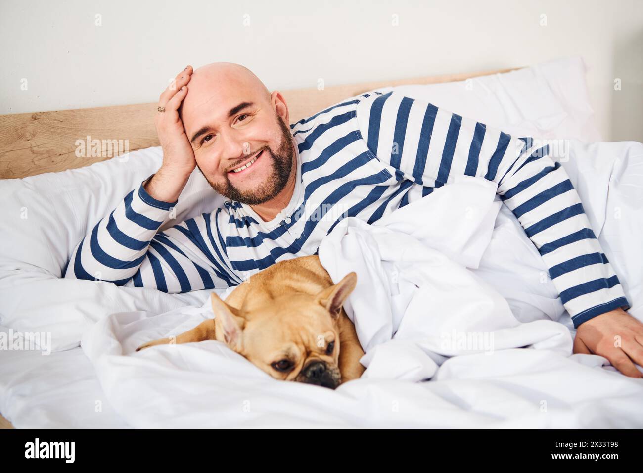 Ein Mann, der friedlich im Bett mit seiner geliebten französischen Bulldogge neben sich ruht. Stockfoto