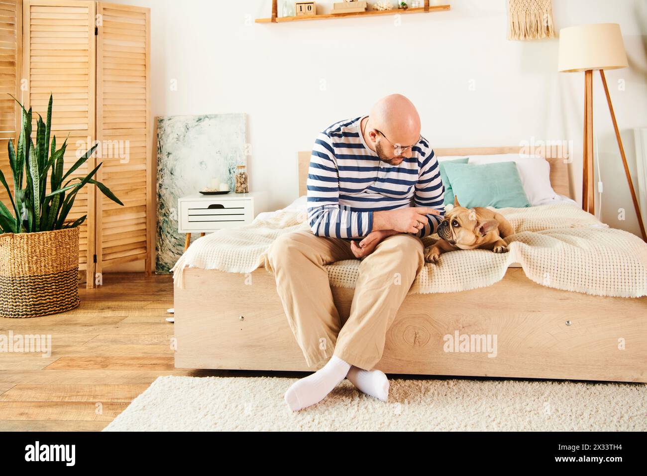 Gutaussehender Mann, der auf dem Bett sitzt und sich mit treuer französischer Bulldogge entspannt. Stockfoto