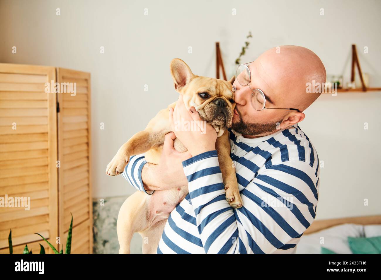 Hübscher Mann mit Brille, der eine kleine französische Bulldogge in den Armen hält. Stockfoto