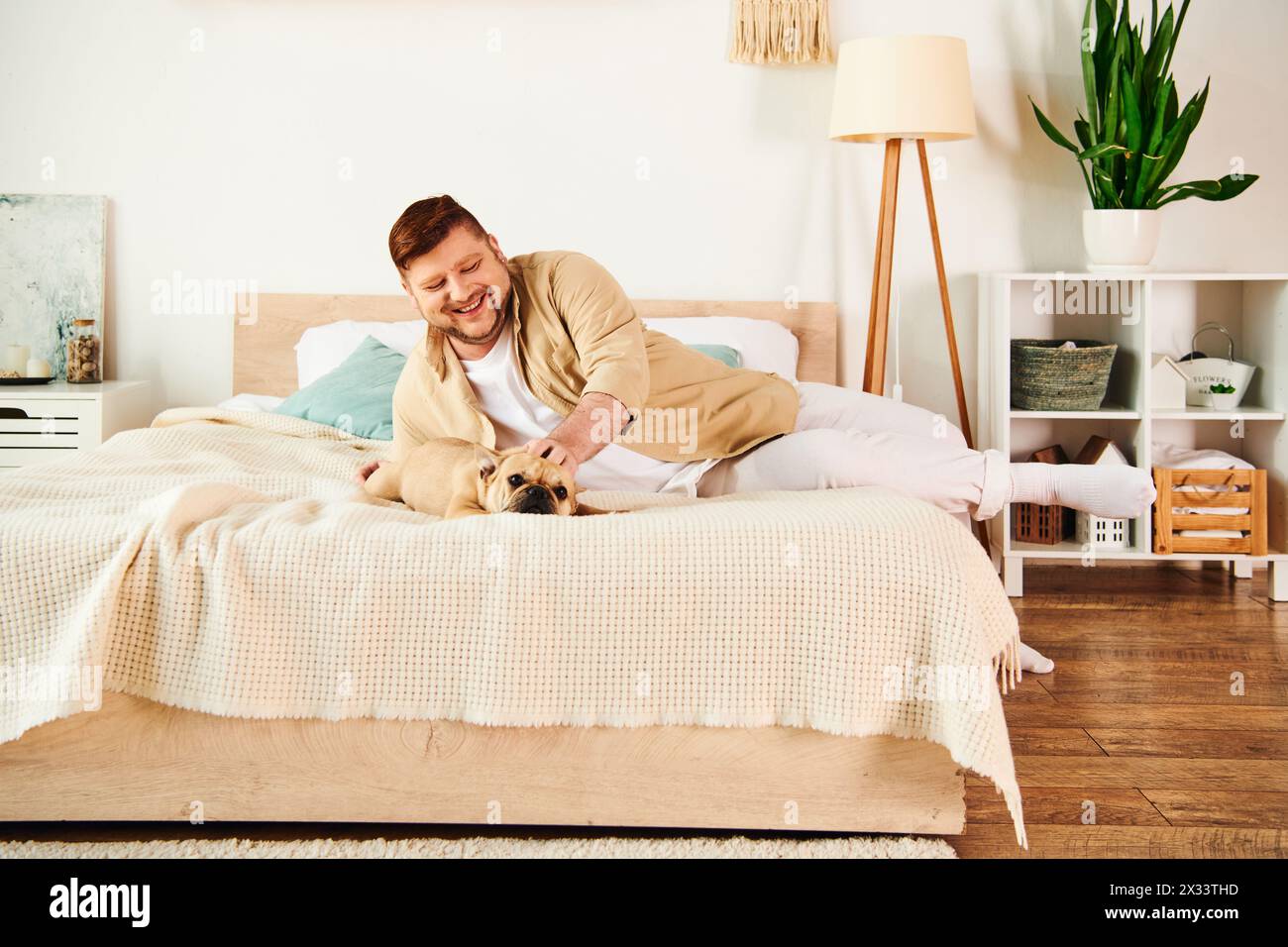 Ein gutaussehender Mann, der sich mit seiner französischen Bulldogge auf einem Bett entspannt. Stockfoto