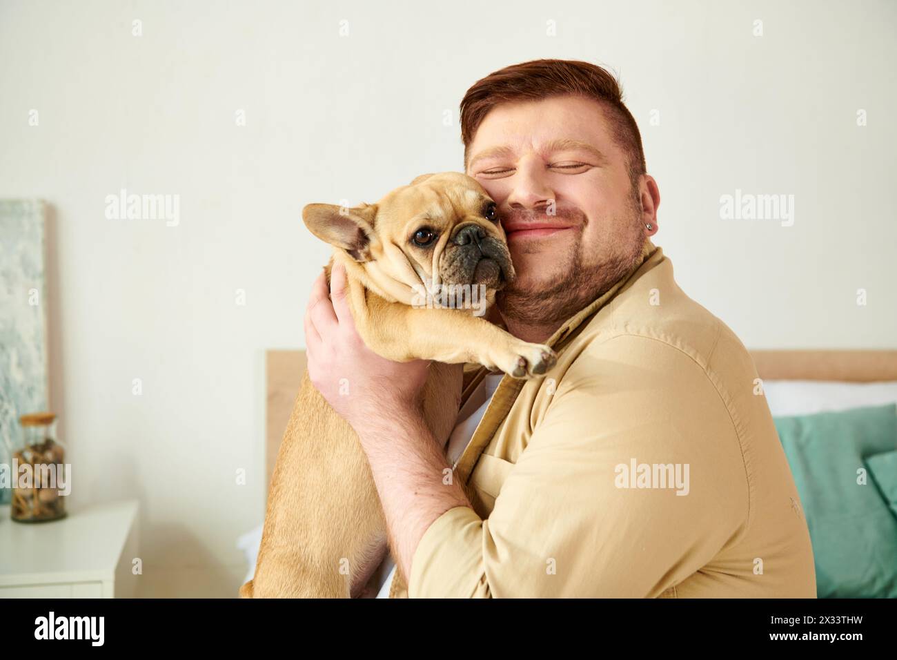 Gutaussehender Mann wiegt zu Hause eine kleine französische Bulldogge in den Armen. Stockfoto