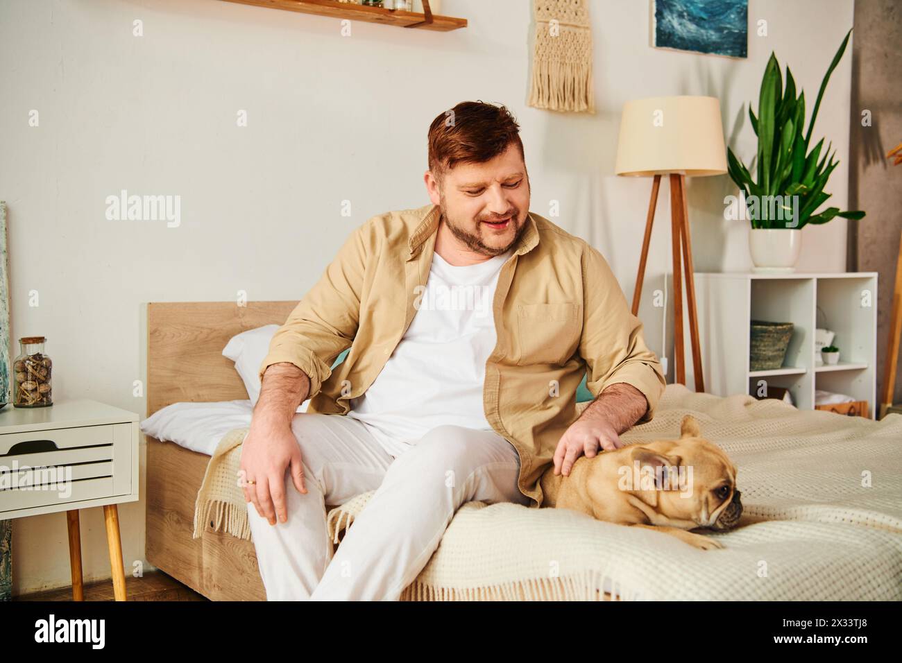 Ein gutaussehender Mann entspannt sich auf einem Bett mit seiner treuen französischen Bulldogge. Stockfoto
