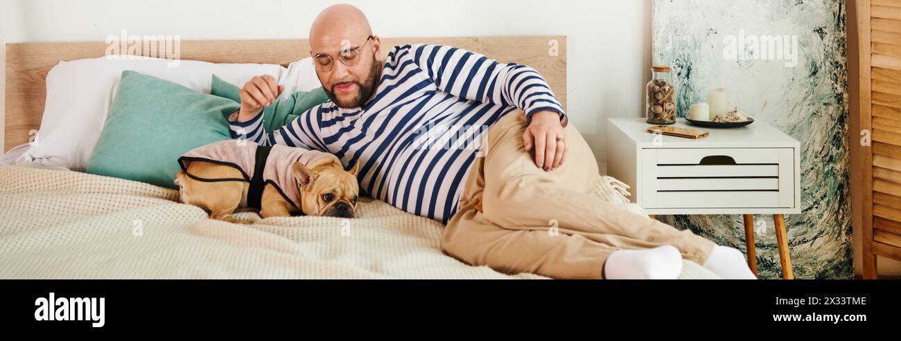 Gutaussehender Mann mit Brille liegt friedlich neben seiner französischen Bulldogge auf einem gemütlichen Bett. Stockfoto