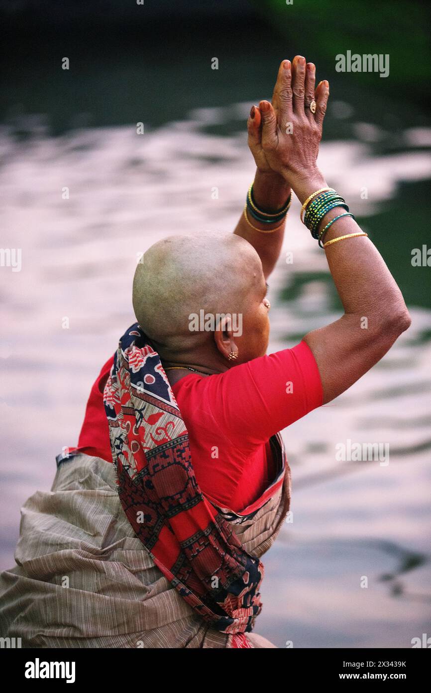 Pilgerfrau mit geschliffenem Kopf, die die Sonne am Ganes River in Varanasi, Indien, grüßt Stockfoto