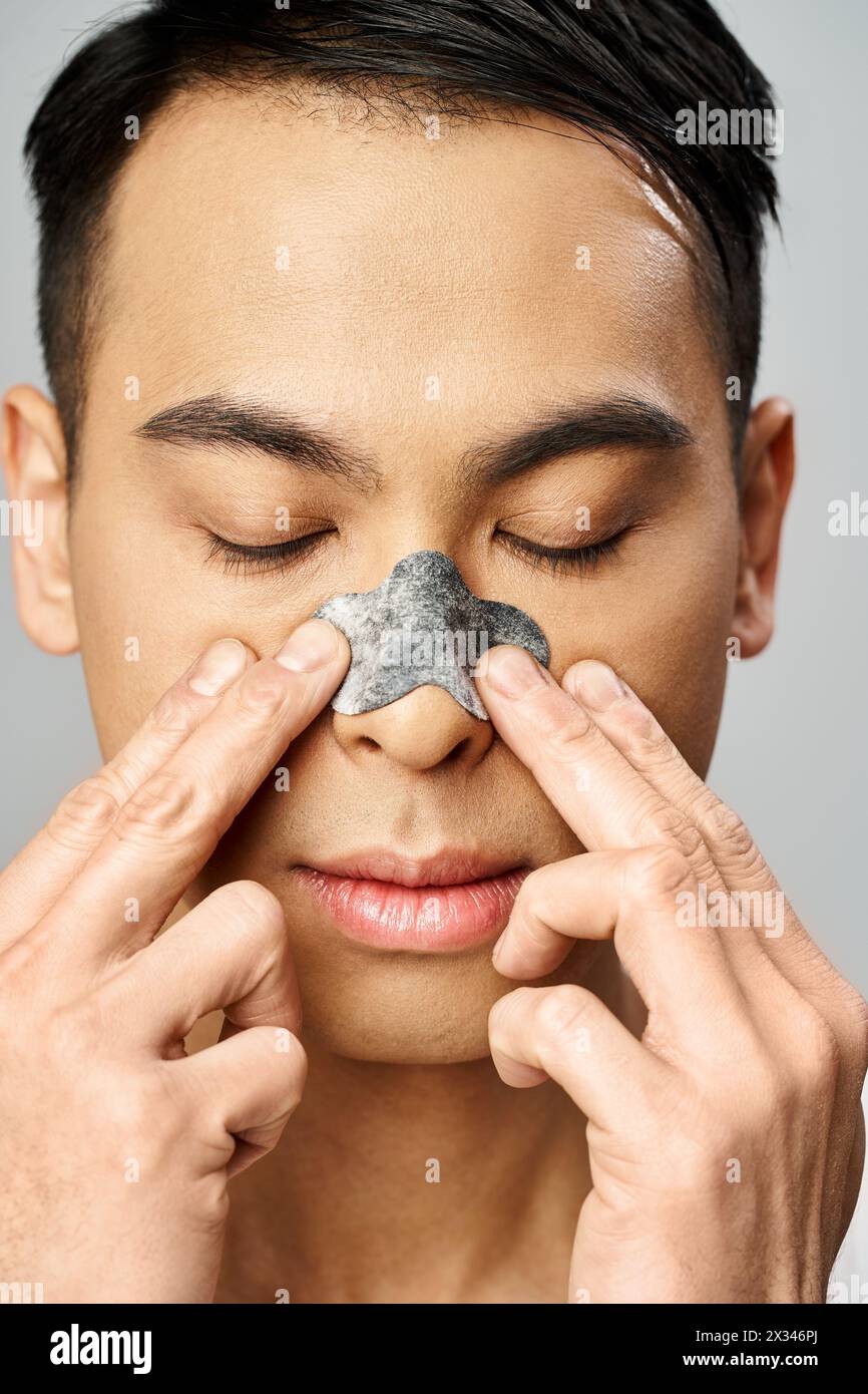 Ein asiatischer Mann mit Nasenaufnäher während seiner Schönheitsroutine in einem grauen Atelier. Stockfoto
