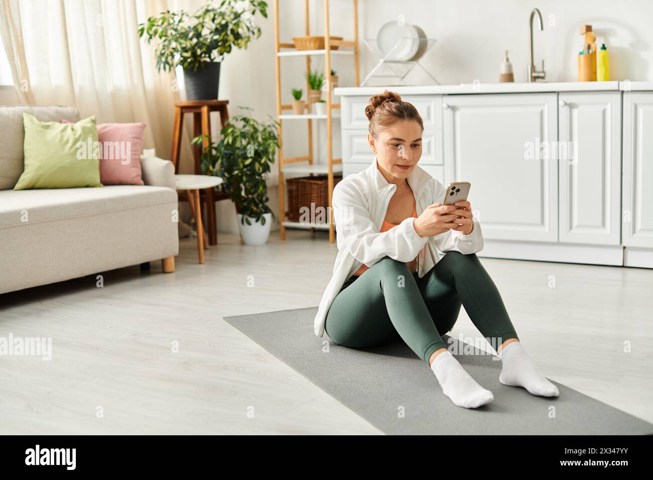 Frau mittleren Alters auf Yogamatte, vertieft in Smartphone. Stockfoto