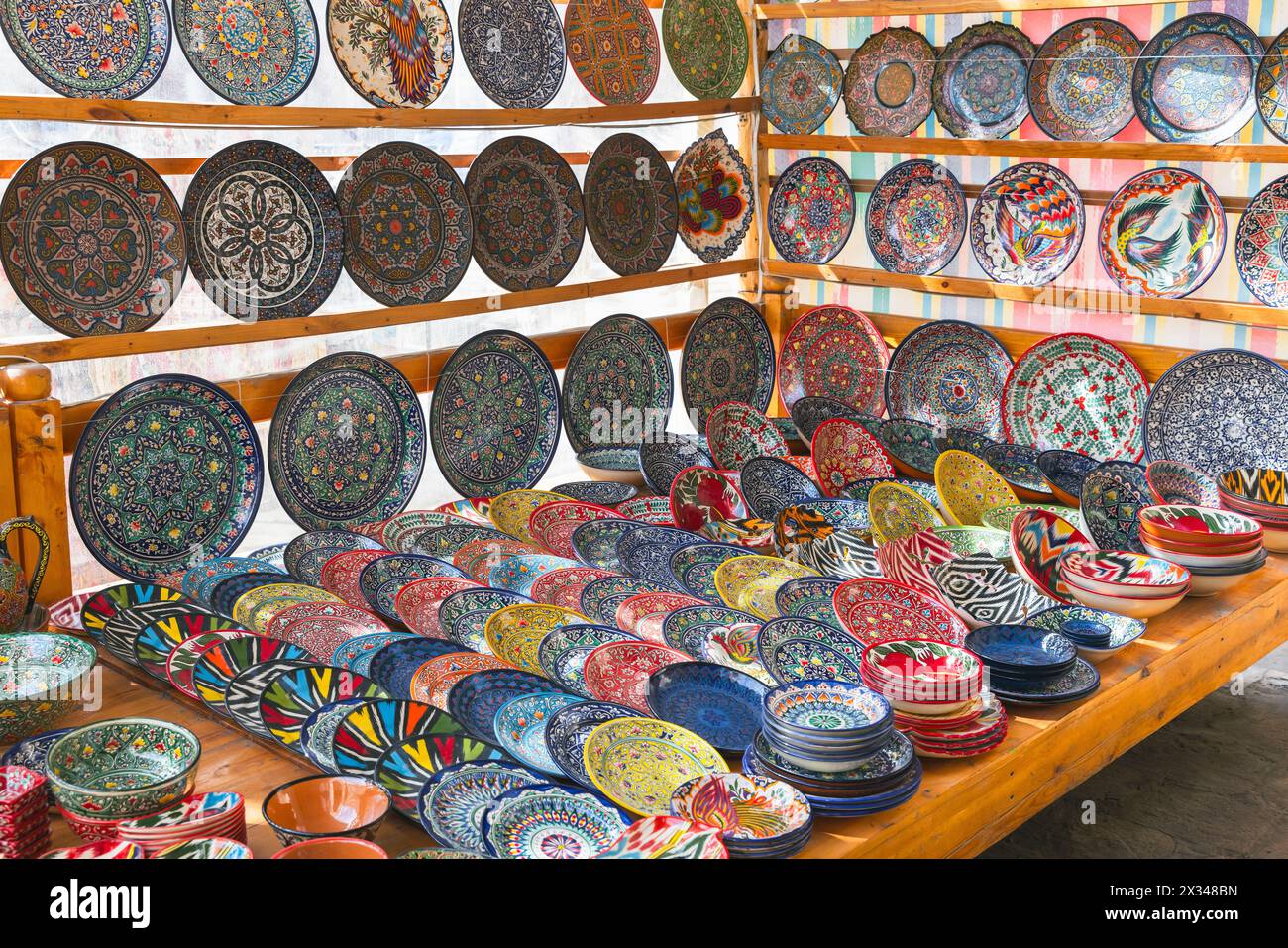 Eine Auswahl handgefertigter usbekischer Teller und Schüsseln mit bunten traditionellen Mustern wird auf einem Straßenmarkt in Buchara verkauft Stockfoto
