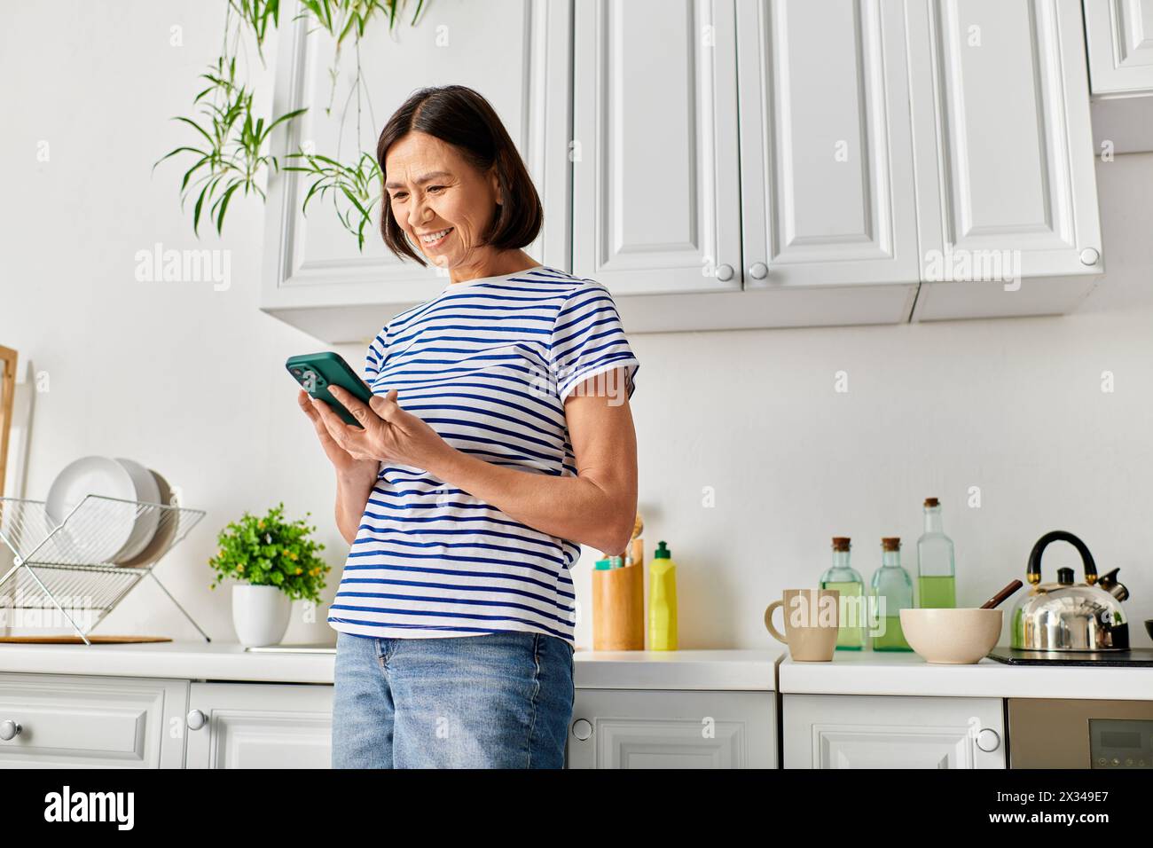 Eine Frau in kuscheliger Hauswäsche steht in einer Küche und hält ein Tablet. Stockfoto Eine Frau in kuscheliger Hauswäsche steht in einer Küche und hält ein Tablet. Stockfoto