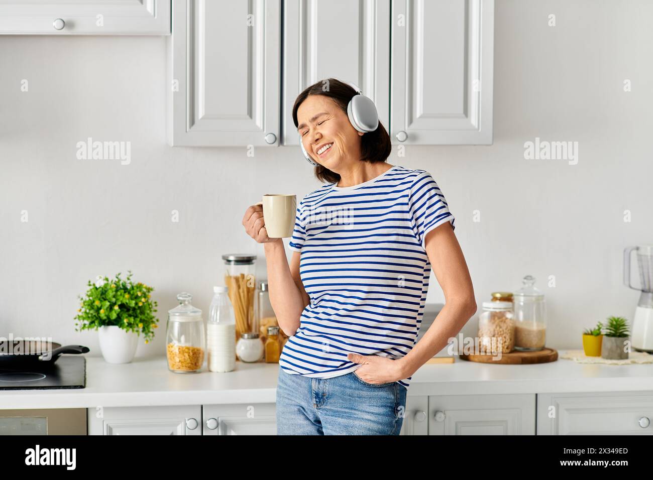 Eine Frau in gemütlicher Hauswäsche, die in einer Küche steht und eine Tasse Kaffee hält. Stockfoto Eine Frau in gemütlicher Hauswäsche, die in einer Küche steht und eine Tasse Kaffee hält. Stockfoto