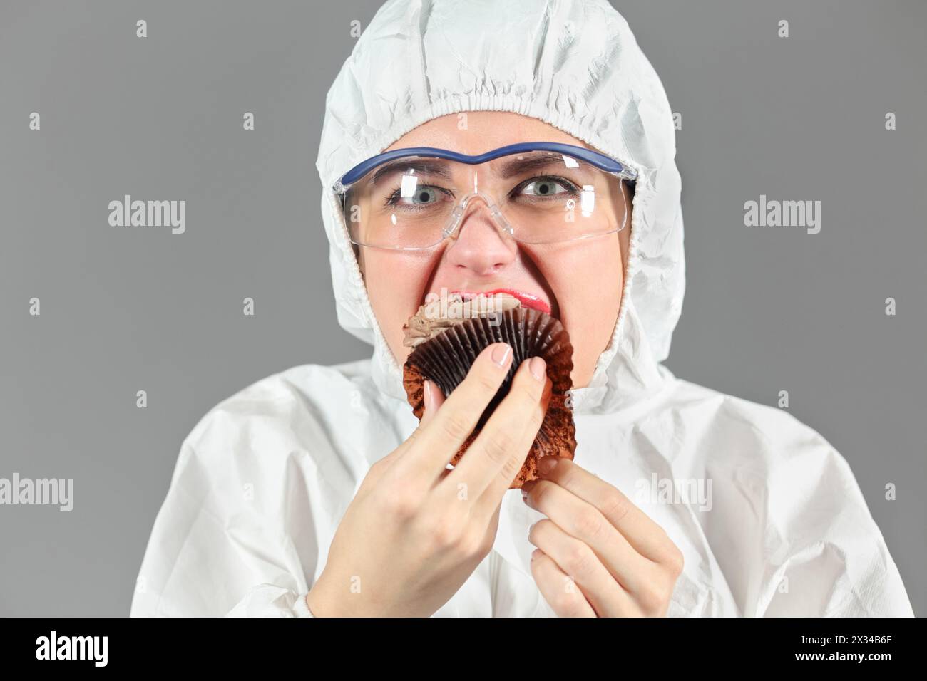 Halblanges Porträt einer Frau, die ein Stück leckeren Schokoladenkuchen beißt und uns ansieht, auf grauem Hintergrund Stockfoto