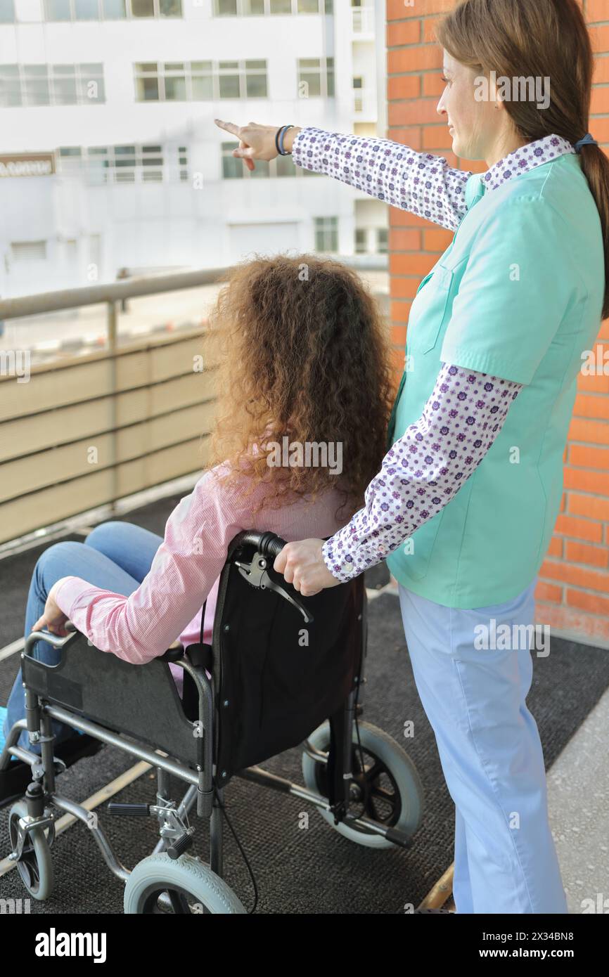 Krankenschwester und Patient im Rollstuhl auf Balkon im Krankenhaus frische Luft atmen, Schwester hielt seine Hand vor dem, was gezeigt wird Stockfoto