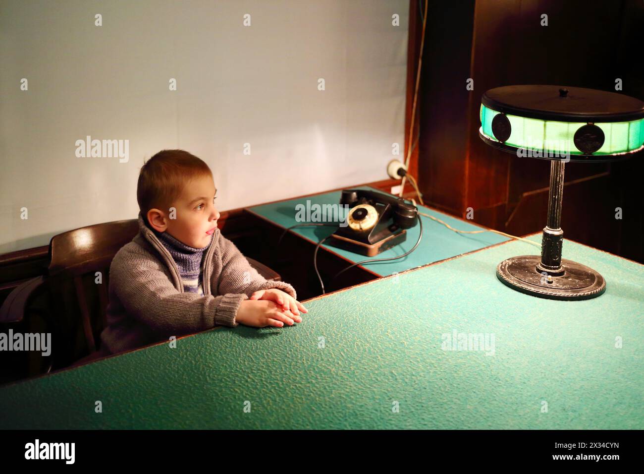 SAMARA, RUSSLAND - 8. MAI 2015: Kleiner Junge (mit Modellfreigabe) sitzt am Tisch mit grünem Tuch und Lampe im Stalins Bunker Stockfoto