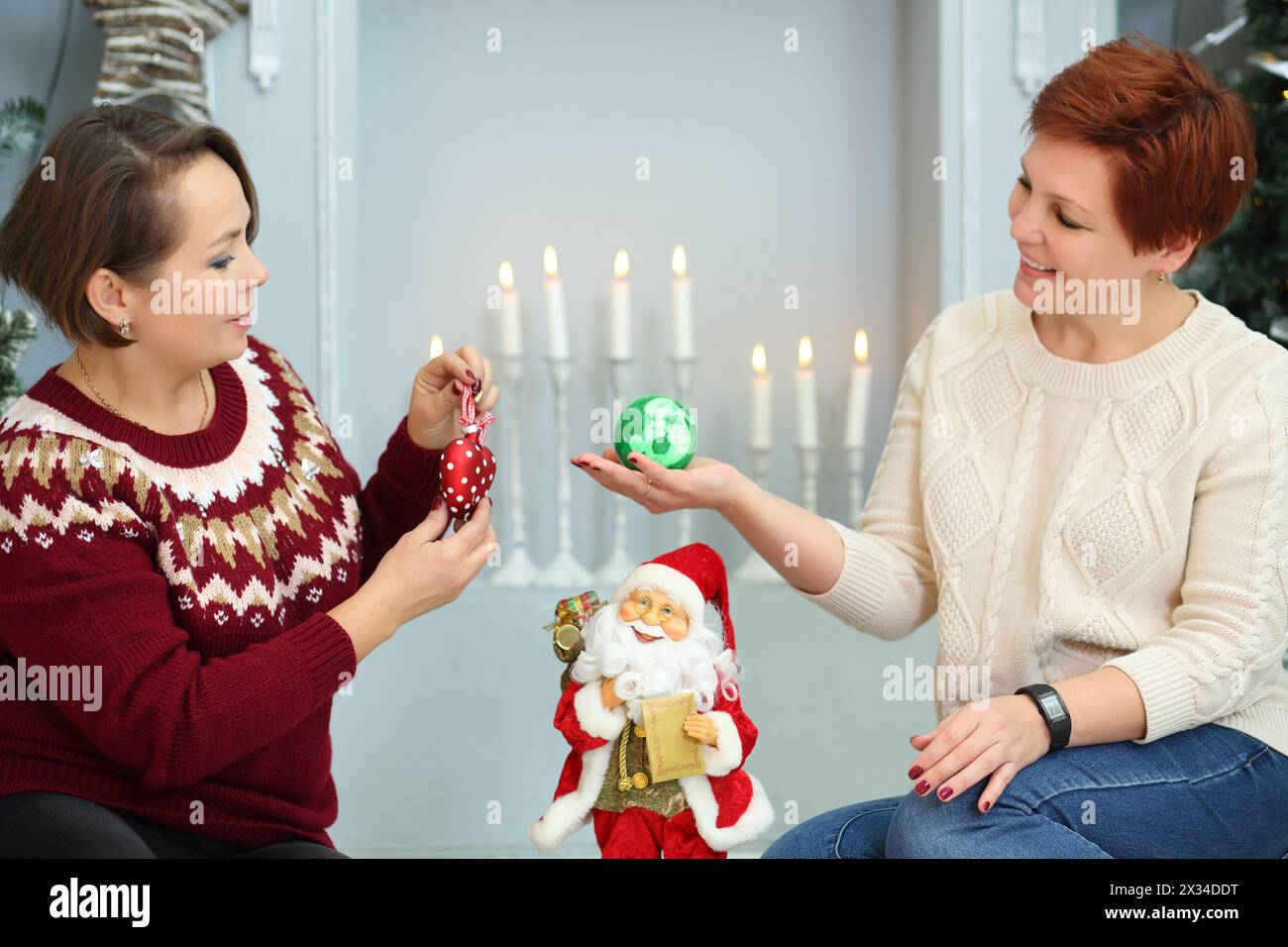 Zwei Frauen sitzen auf dem Boden mit weihnachtskugeln neben dem Kamin mit Kerzen Stockfoto